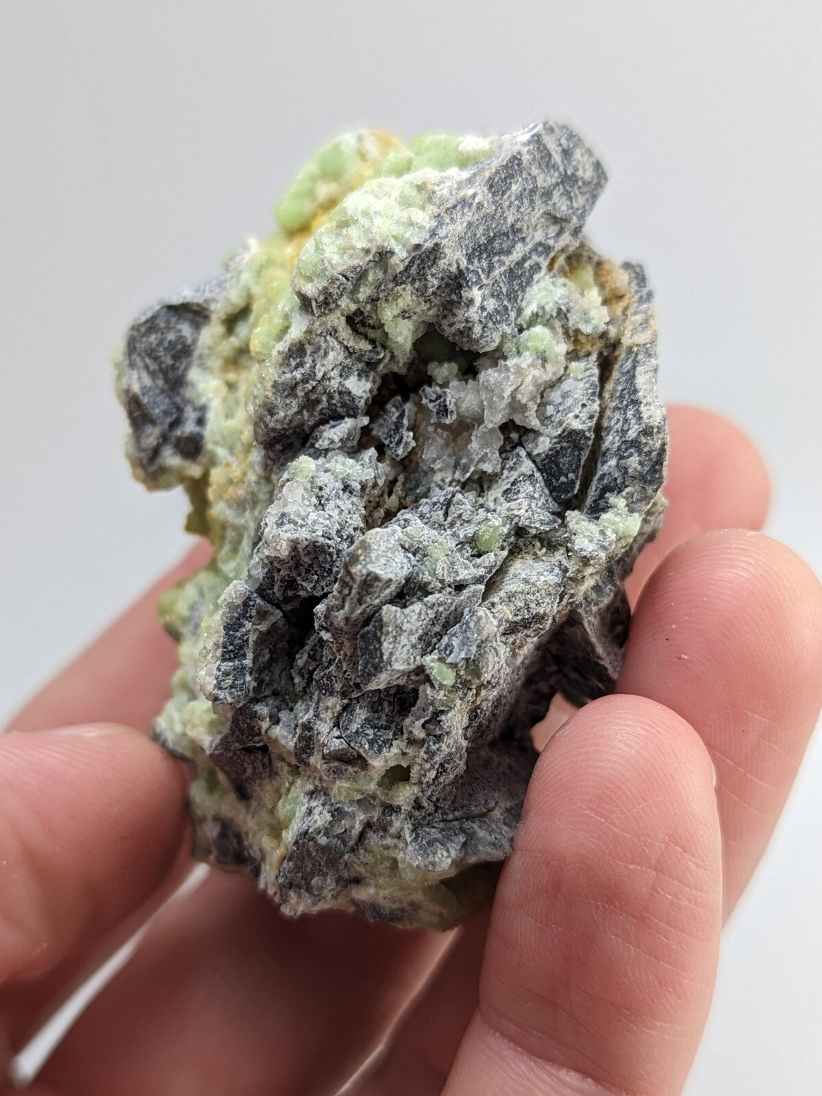 A rough, irregularly shaped mineral specimen with a mottled surface of dark gray and pale green hues.