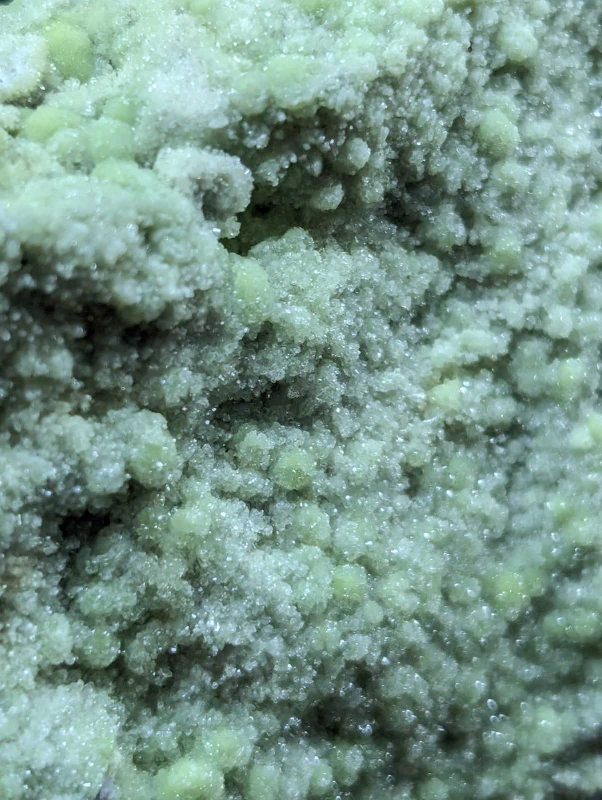 A textured, pale green crystalline substance with a granular and slightly glossy surface.