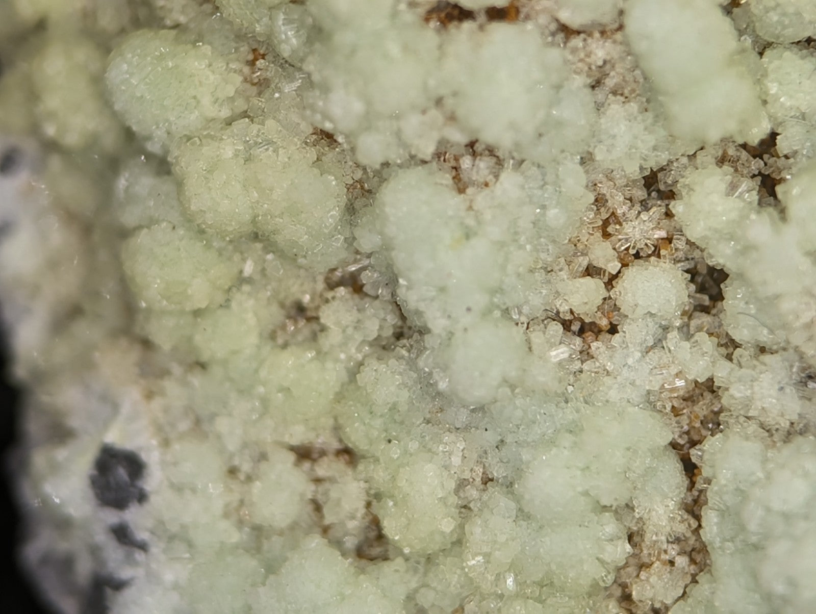 A cluster of translucent, pale greenish-white crystalline formations with a rough, jagged texture and some smaller clear crystals interspersed among them.