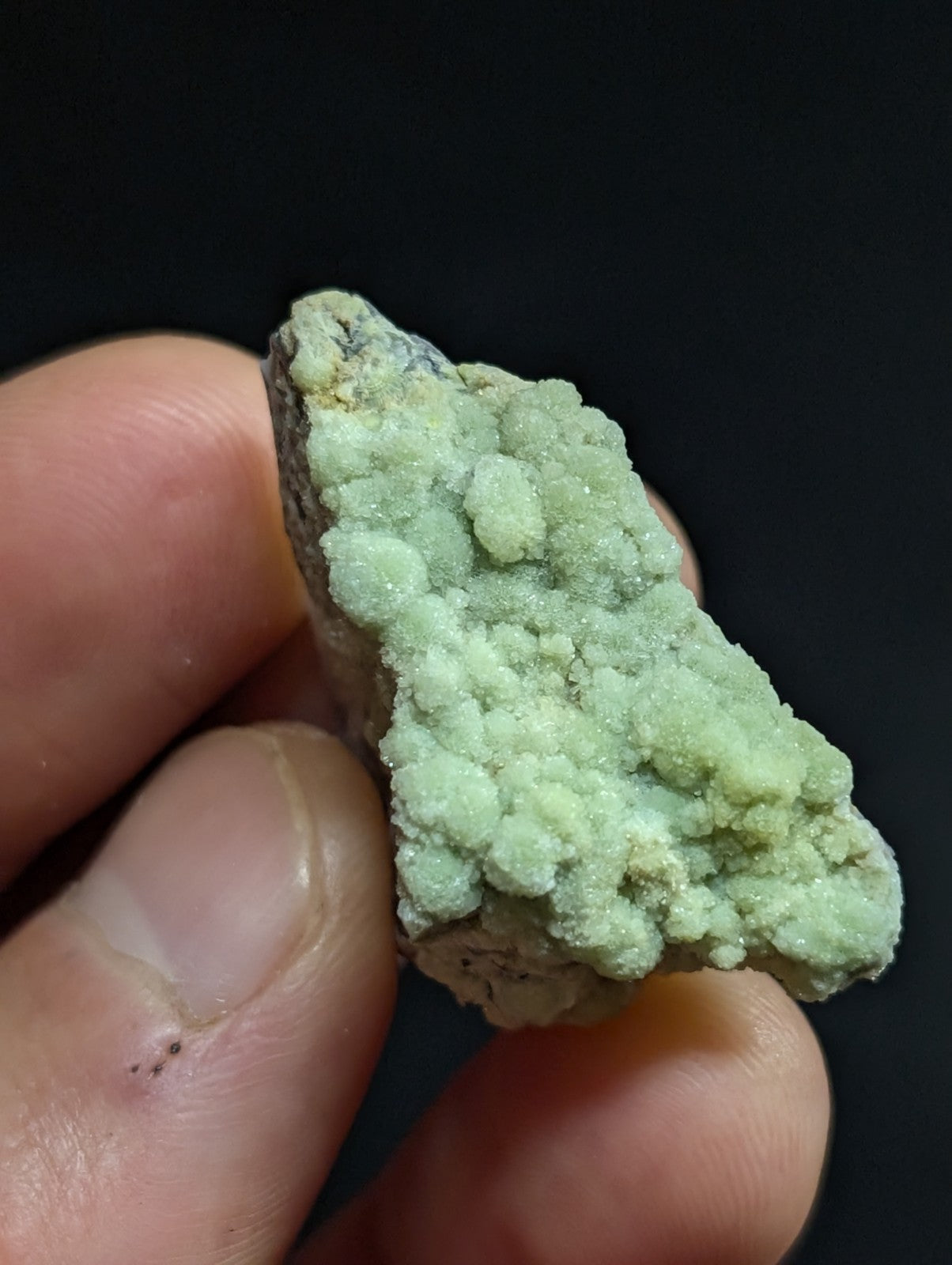 A pale green, crystalline mineral specimen with a rough, textured surface held in someone’s hand.