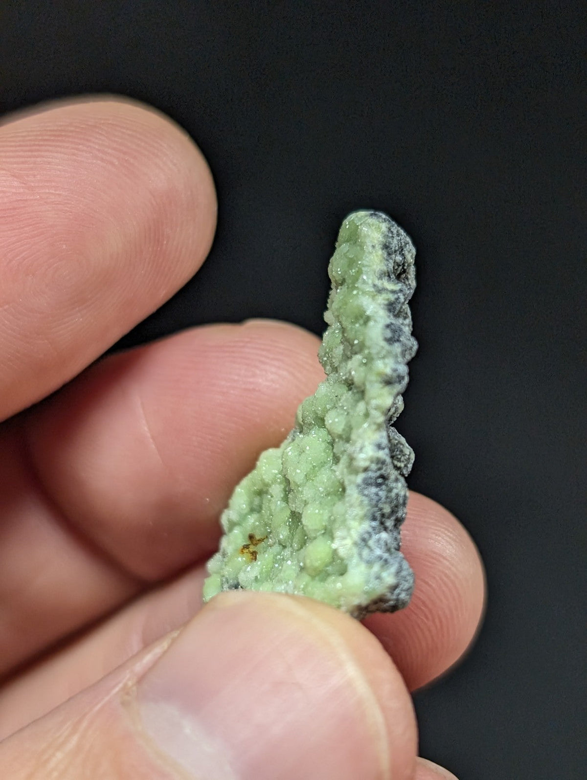 A textured, light green mineral specimen with a rough, bumpy surface and darker grayish patches.