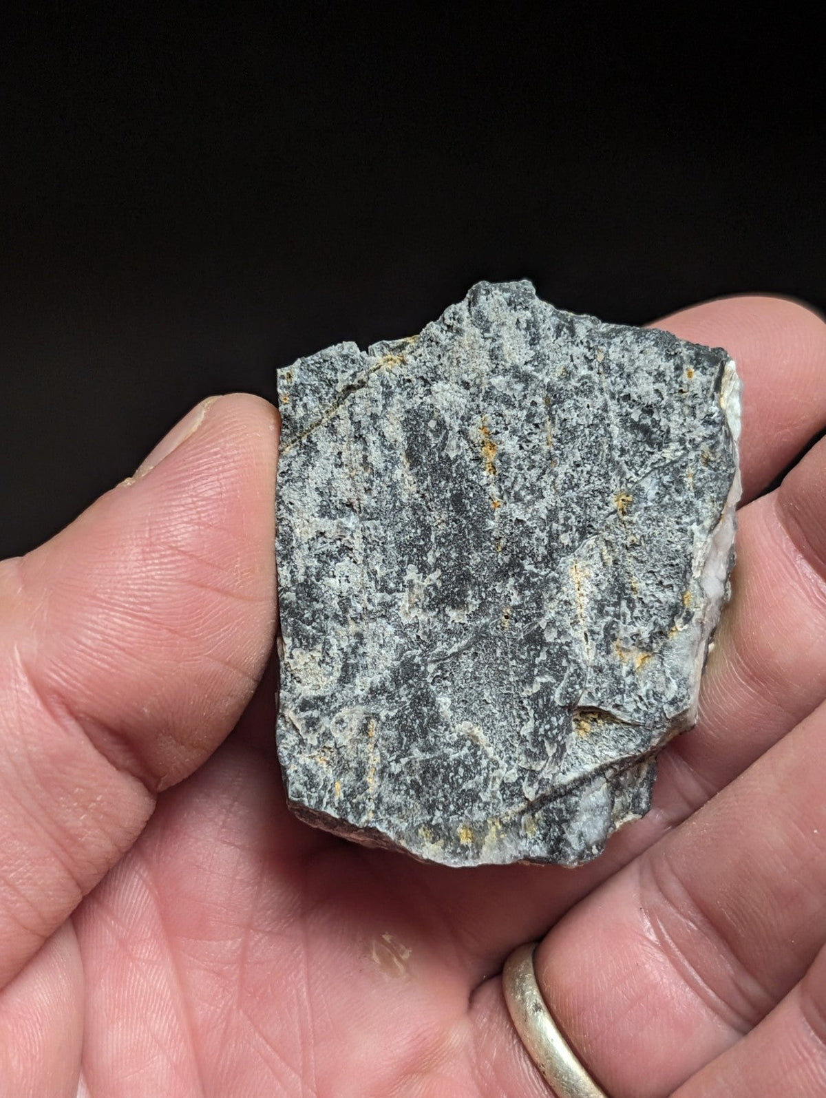 A rough, irregularly shaped gray rock with speckles of white and faint yellow mineral veins.
