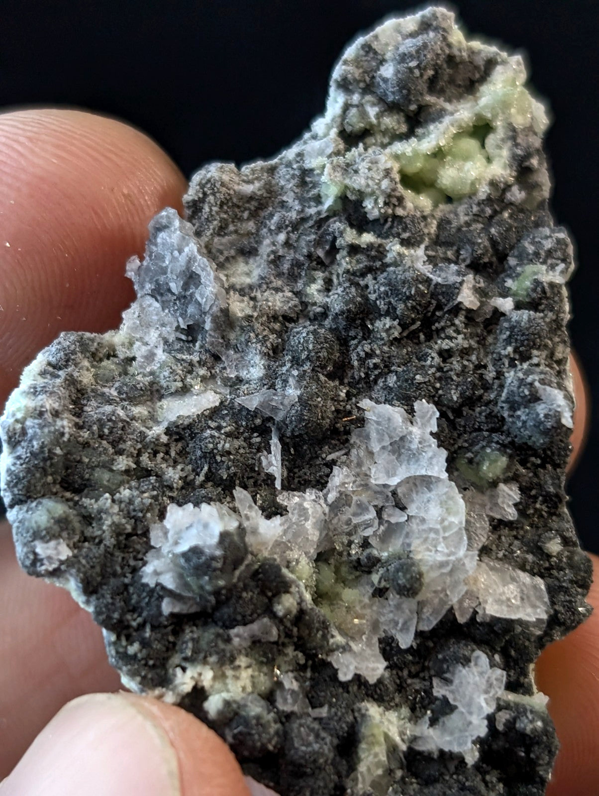 A rugged, dark gray mineral specimen with translucent white crystalline formations and patches of pale green.