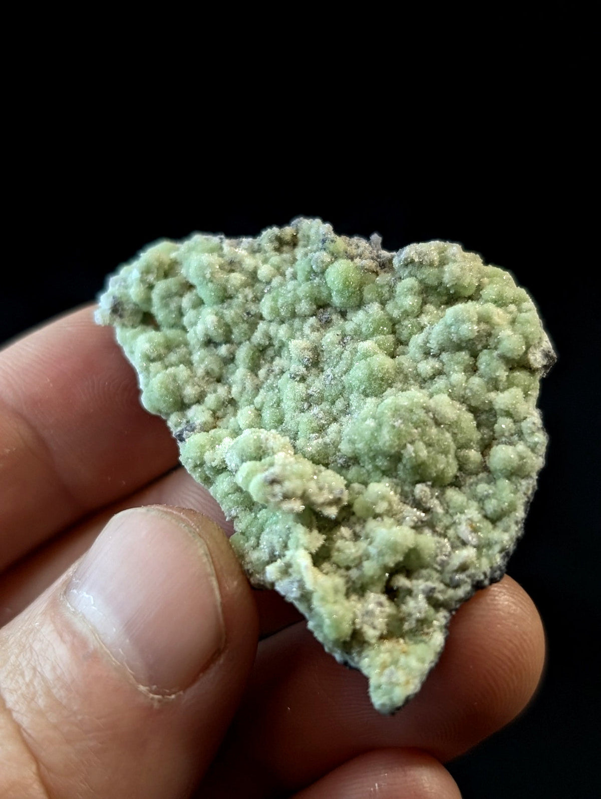 A light green, textured mineral specimen with a bumpy, crystalline surface held in someone’s hand.