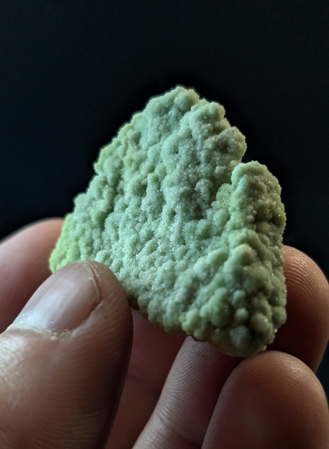 A pale green, textured mineral specimen with a rough, bumpy surface held between fingers.