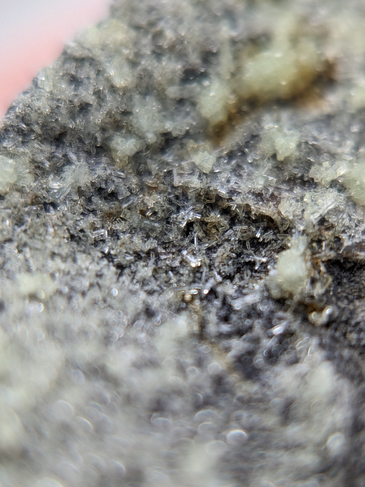 A rough, grayish-black mineral specimen with crystalline textures and scattered translucent white inclusions.