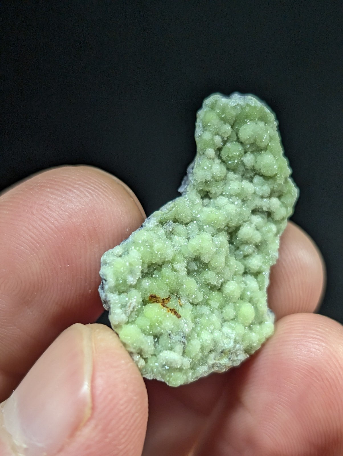 A pale green, textured mineral specimen with a crystalline surface held gently between fingers.