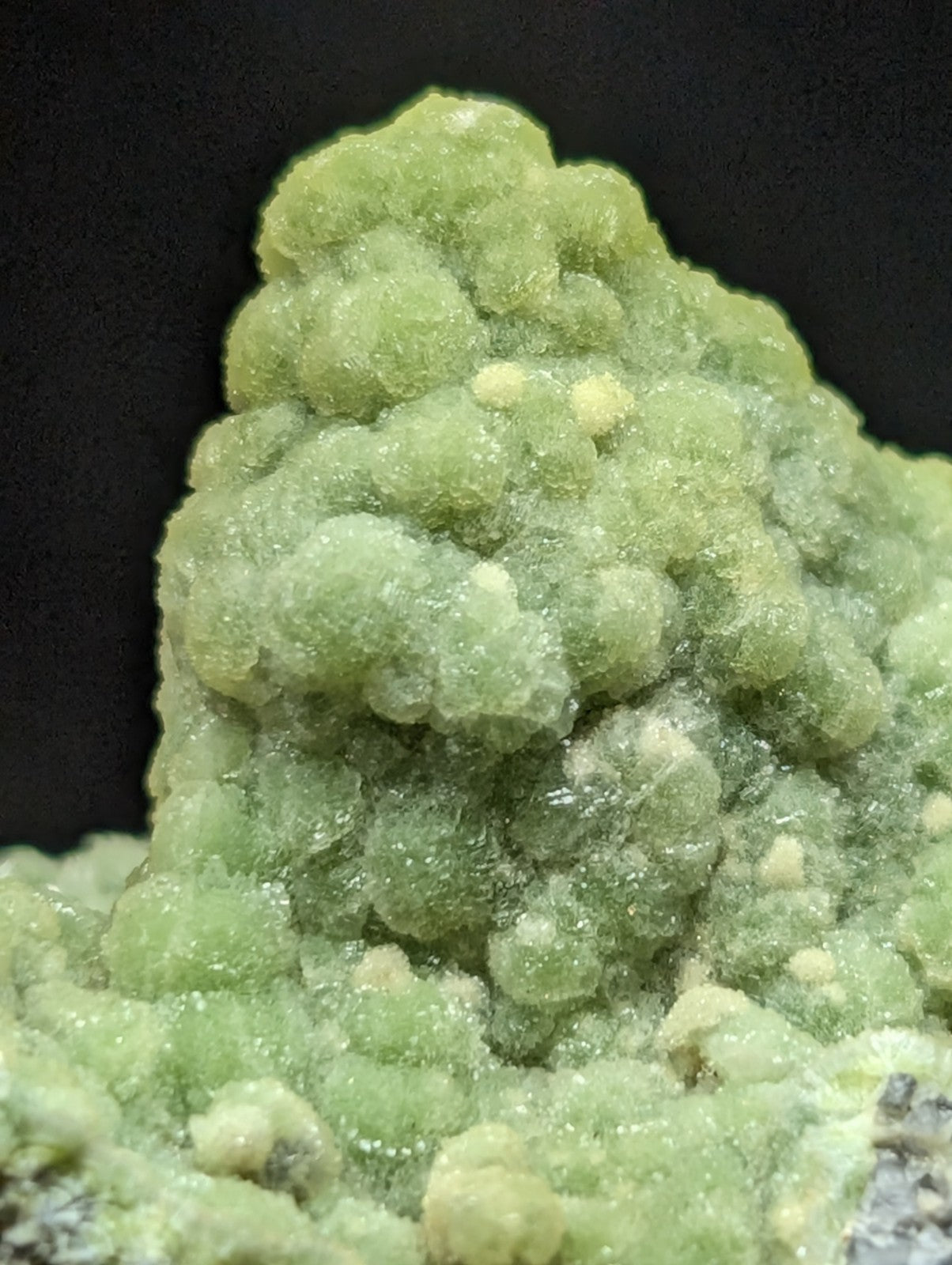 A vibrant green, bubbly mineral specimen with a textured, crystalline surface and subtle yellowish highlights.