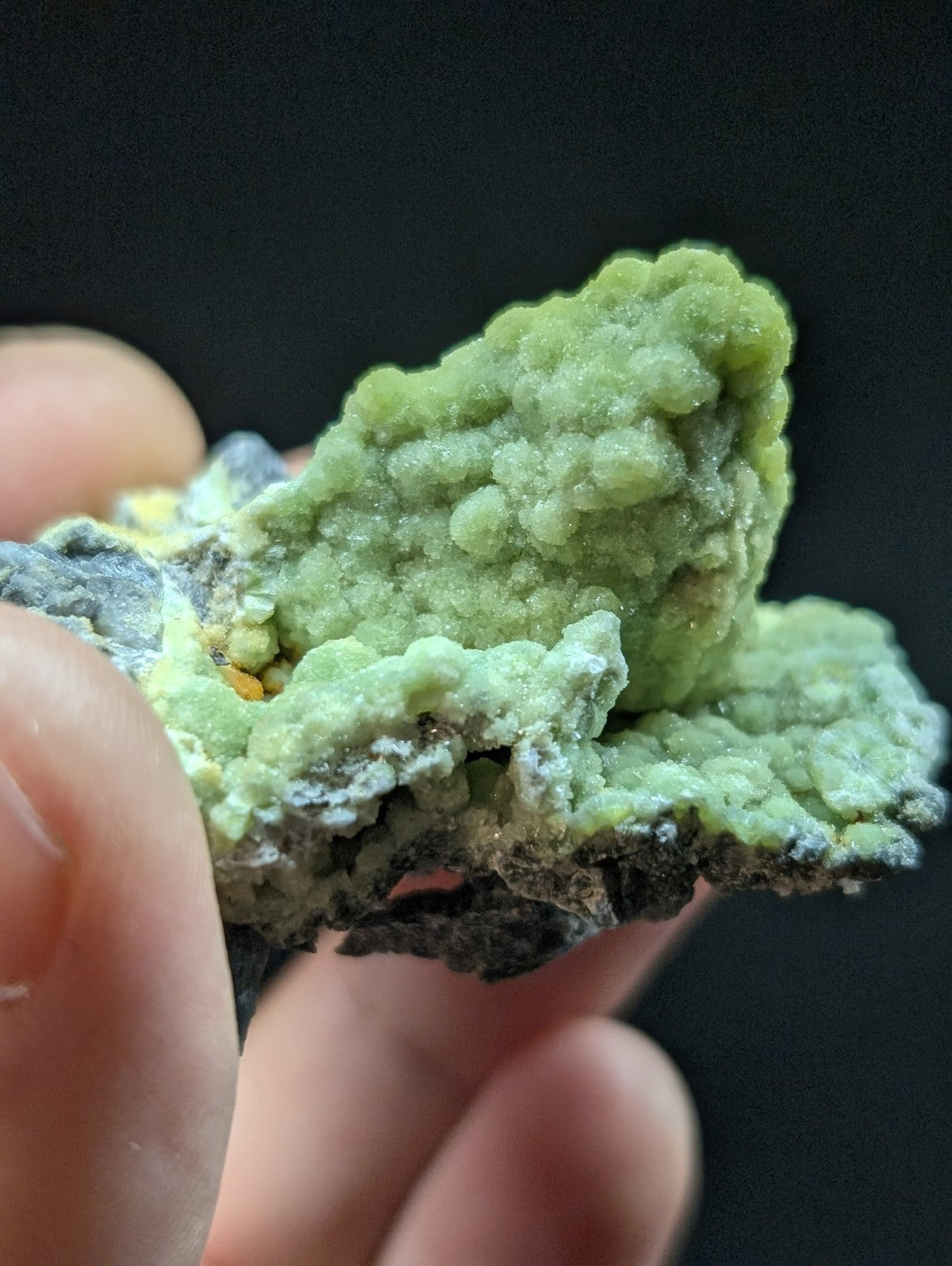 A textured, light green mineral specimen with a bumpy surface and hints of yellow and gray.