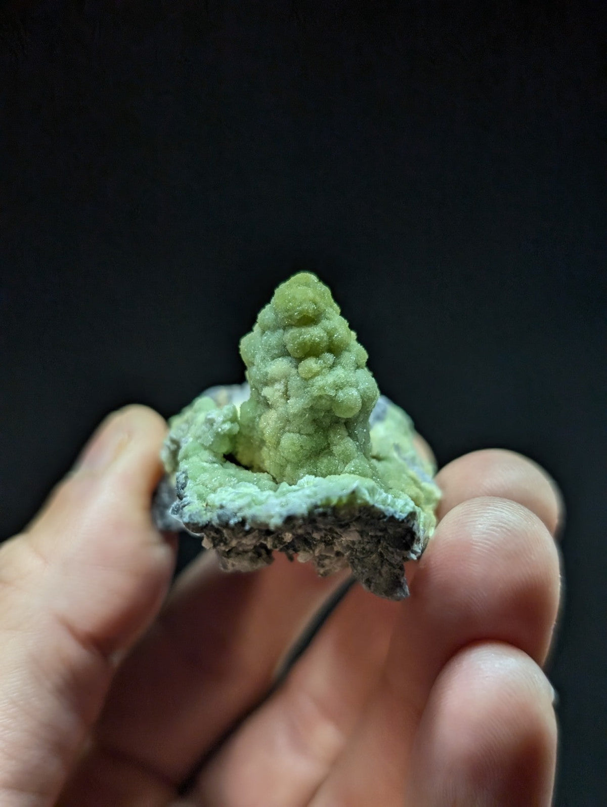 A vibrant green, textured mineral specimen with a bumpy, conical growth emerging from a rougher base.