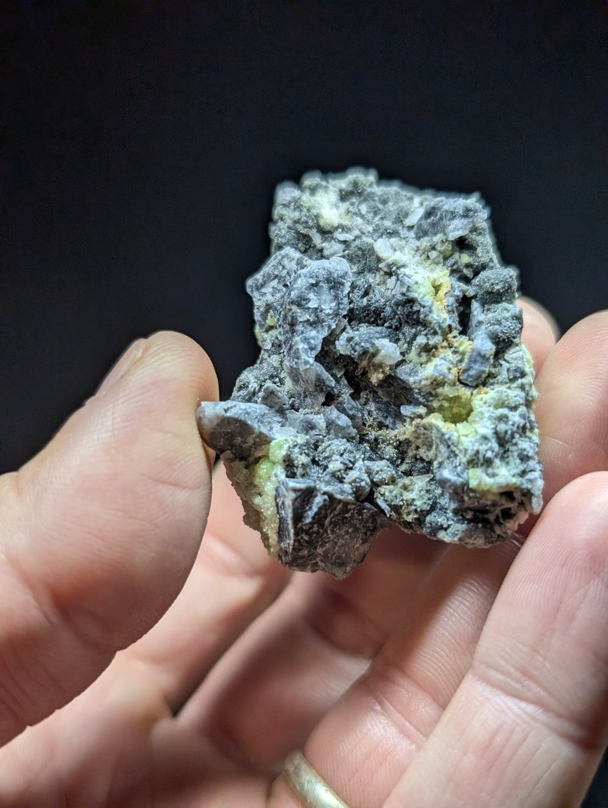 A rugged, irregularly shaped mineral specimen with a mottled gray surface accented by patches of yellow-green.