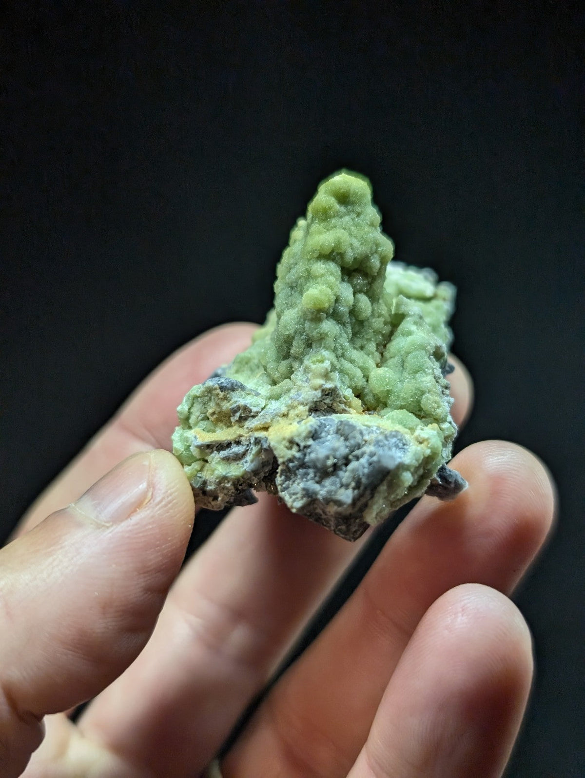 A textured, light green mineral specimen with a rough, bumpy surface and patches of grayish material.