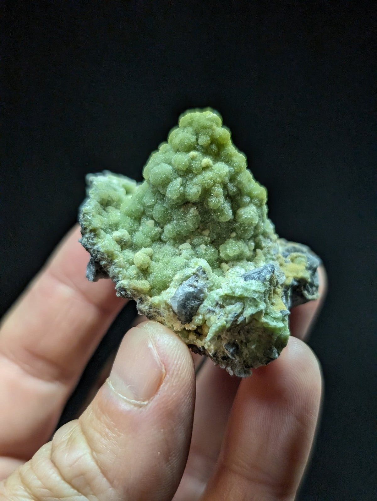 A textured, light green mineral specimen with a bumpy surface and darker grayish patches.