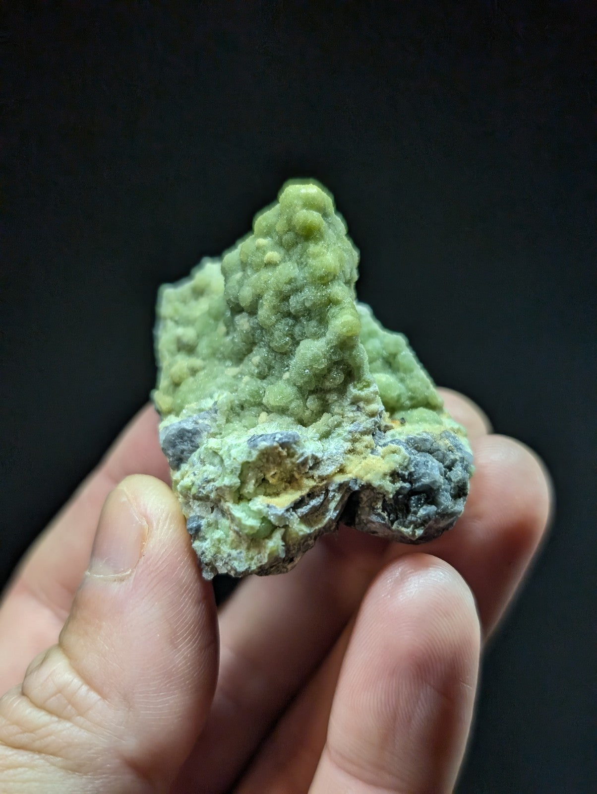 A rough, irregularly shaped green mineral specimen with patches of gray and yellowish hues.