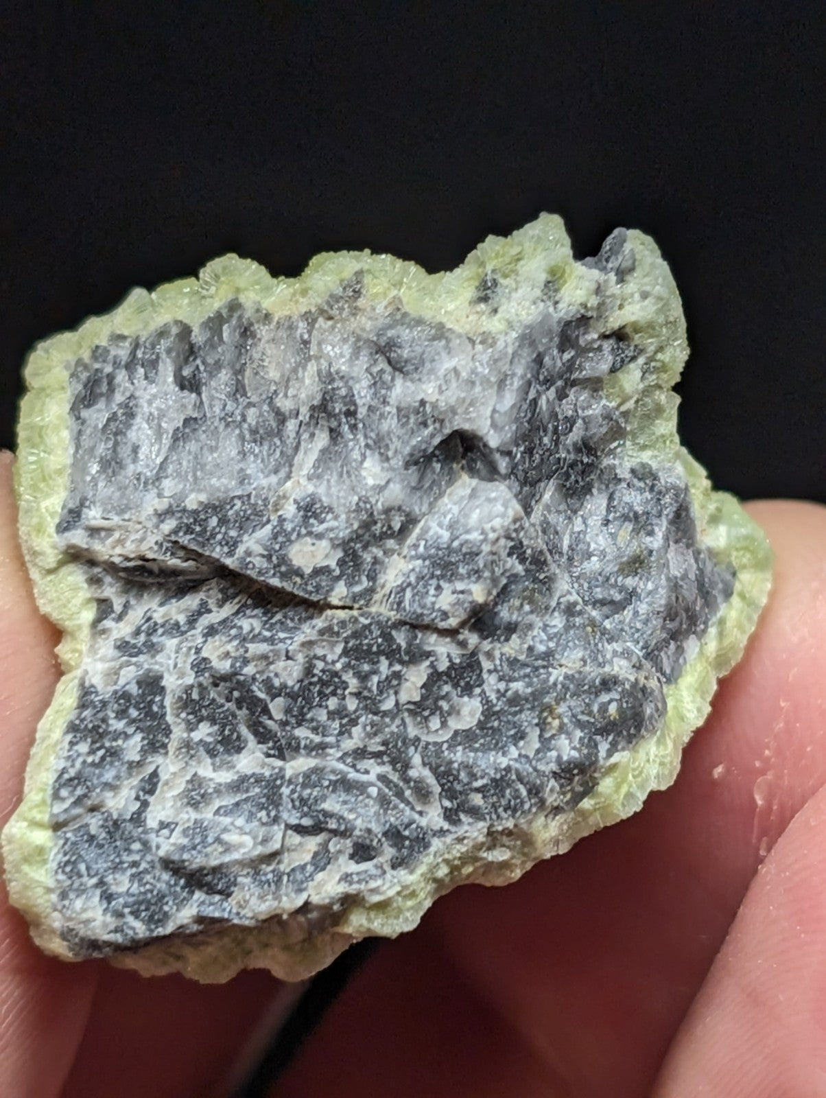 A rough, irregularly shaped mineral specimen with a pale green outer matrix and a darker grayish interior featuring mottled patterns.