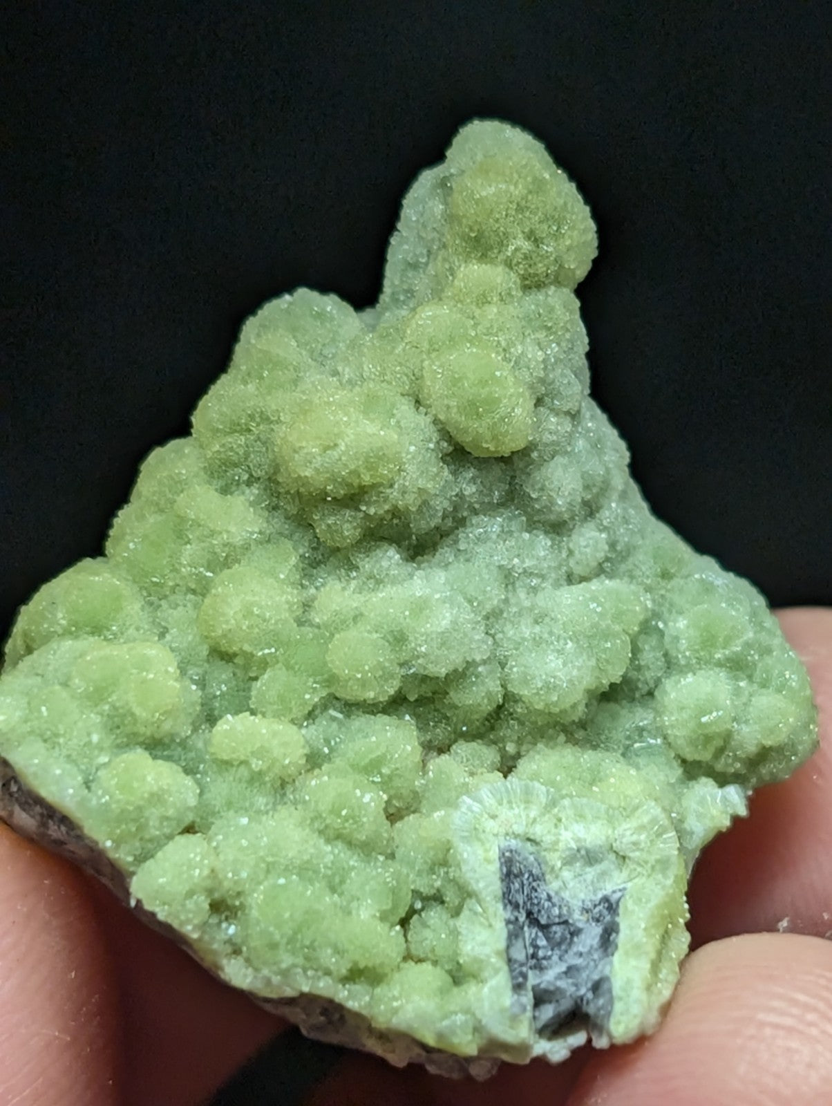 A vibrant green, crystalline mineral specimen with a textured, bumpy surface and a dark gray inclusion.