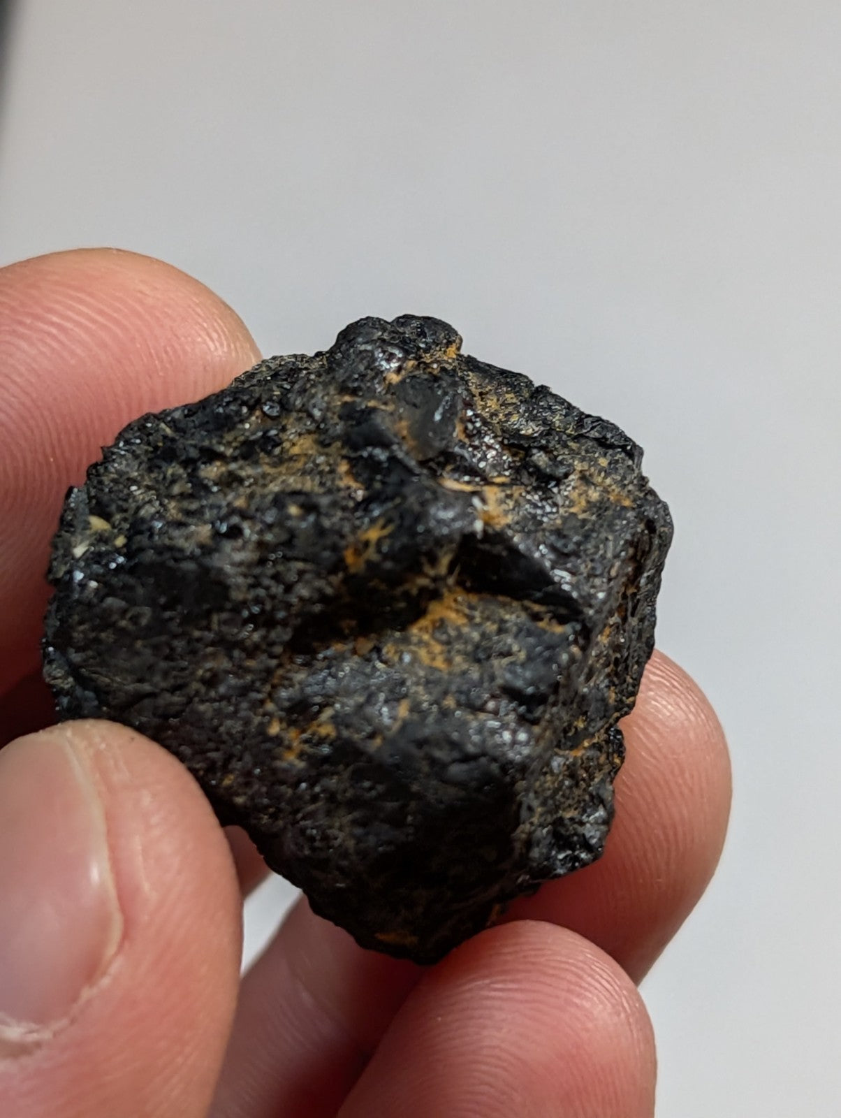 A rugged, dark metallic meteorite with patches of golden-yellow mineral inclusions.
