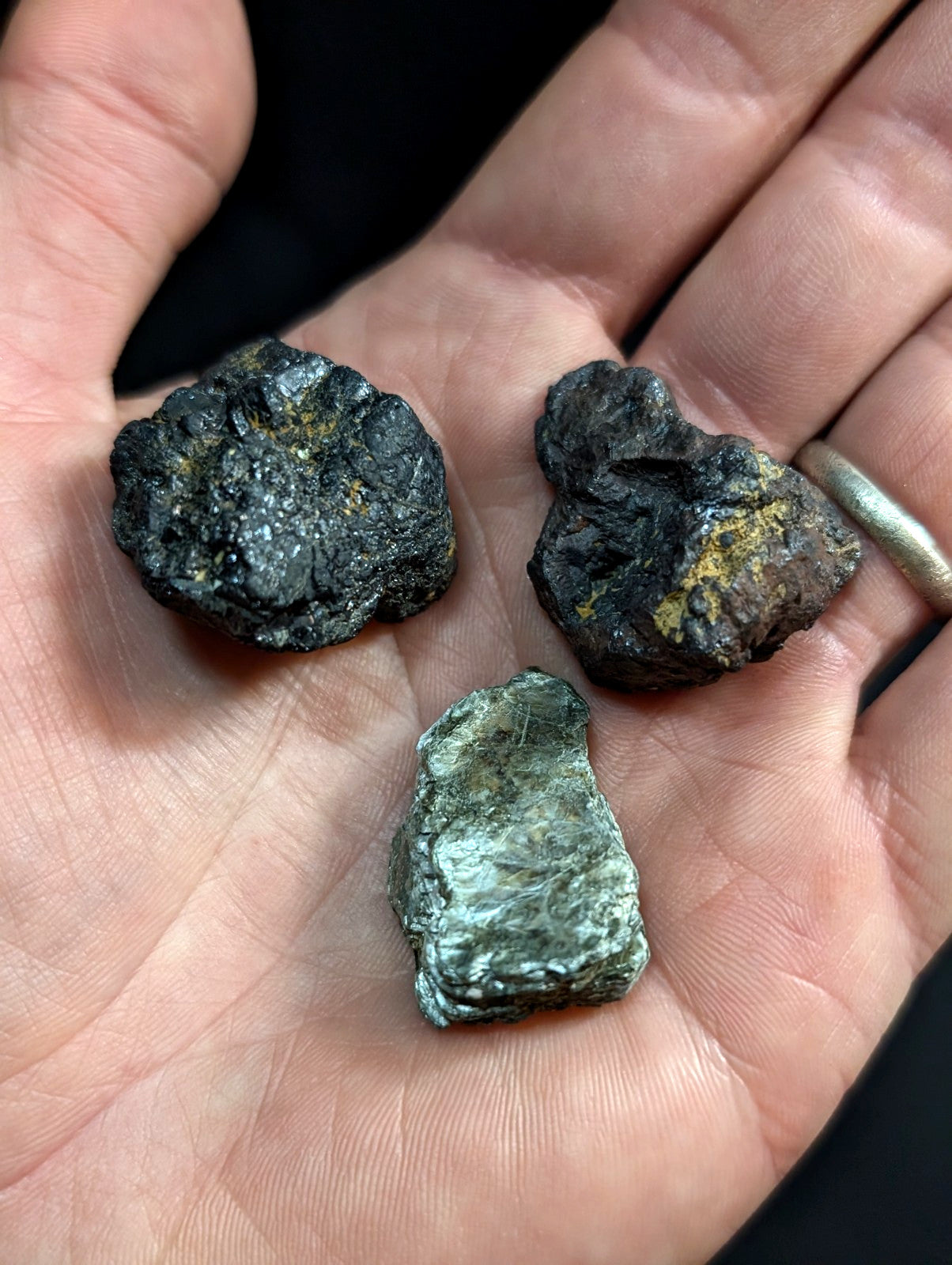 Three irregularly shaped, rough-textured mineral specimens with dark metallic surfaces and patches of yellowish-green oxidation.