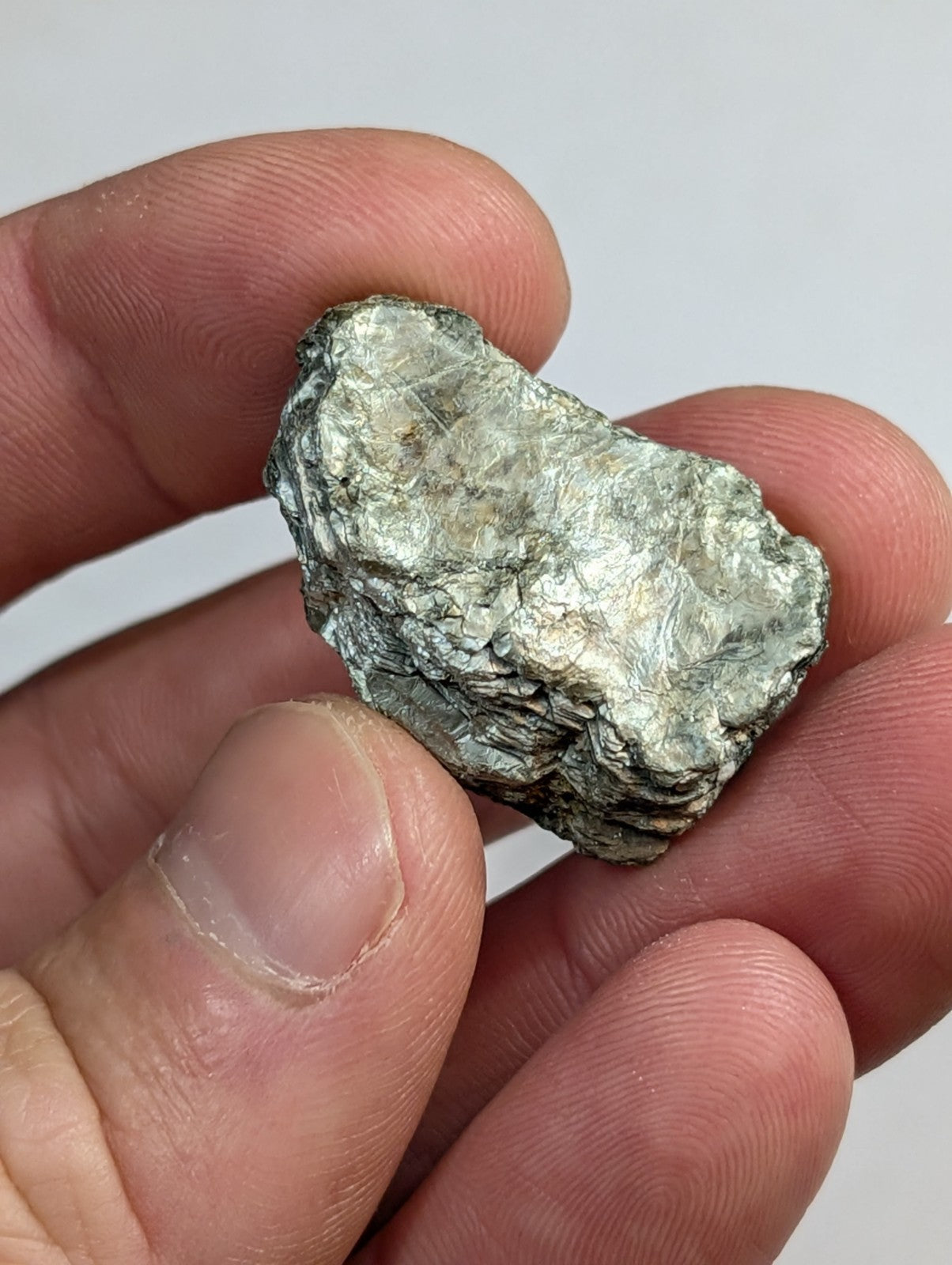 A rough, irregularly shaped metallic mineral specimen with a silvery-gray surface and subtle greenish undertones.