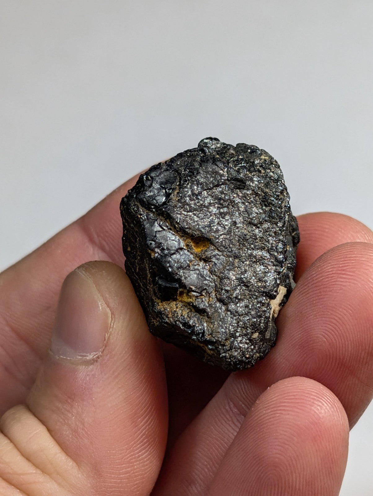 A rugged, dark gray meteorite with a rough, textured surface and subtle hints of yellowish mineral inclusions.