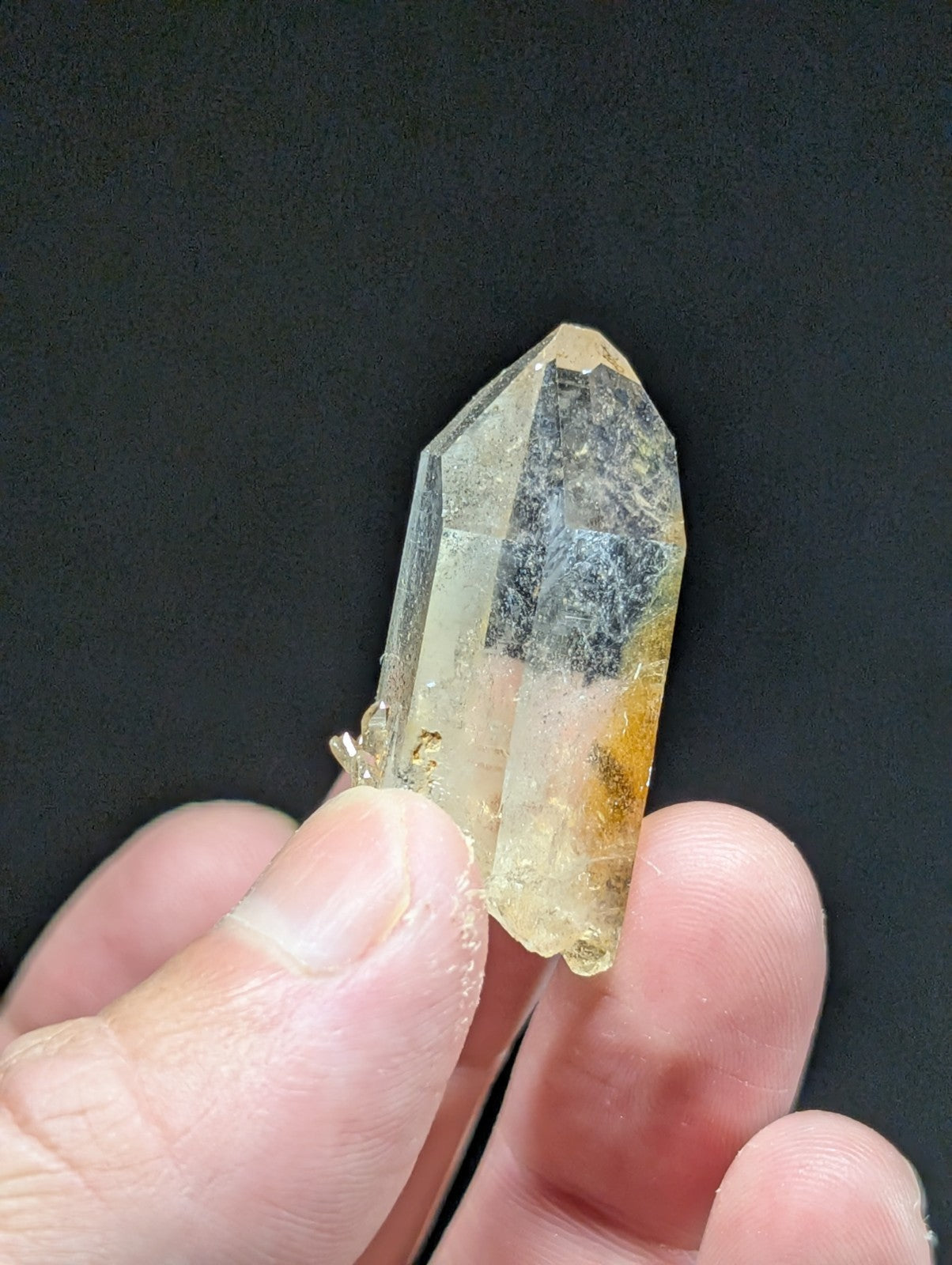 A translucent yellowish quartz crystal with a pointed tip and visible internal inclusions, held gently between fingers.