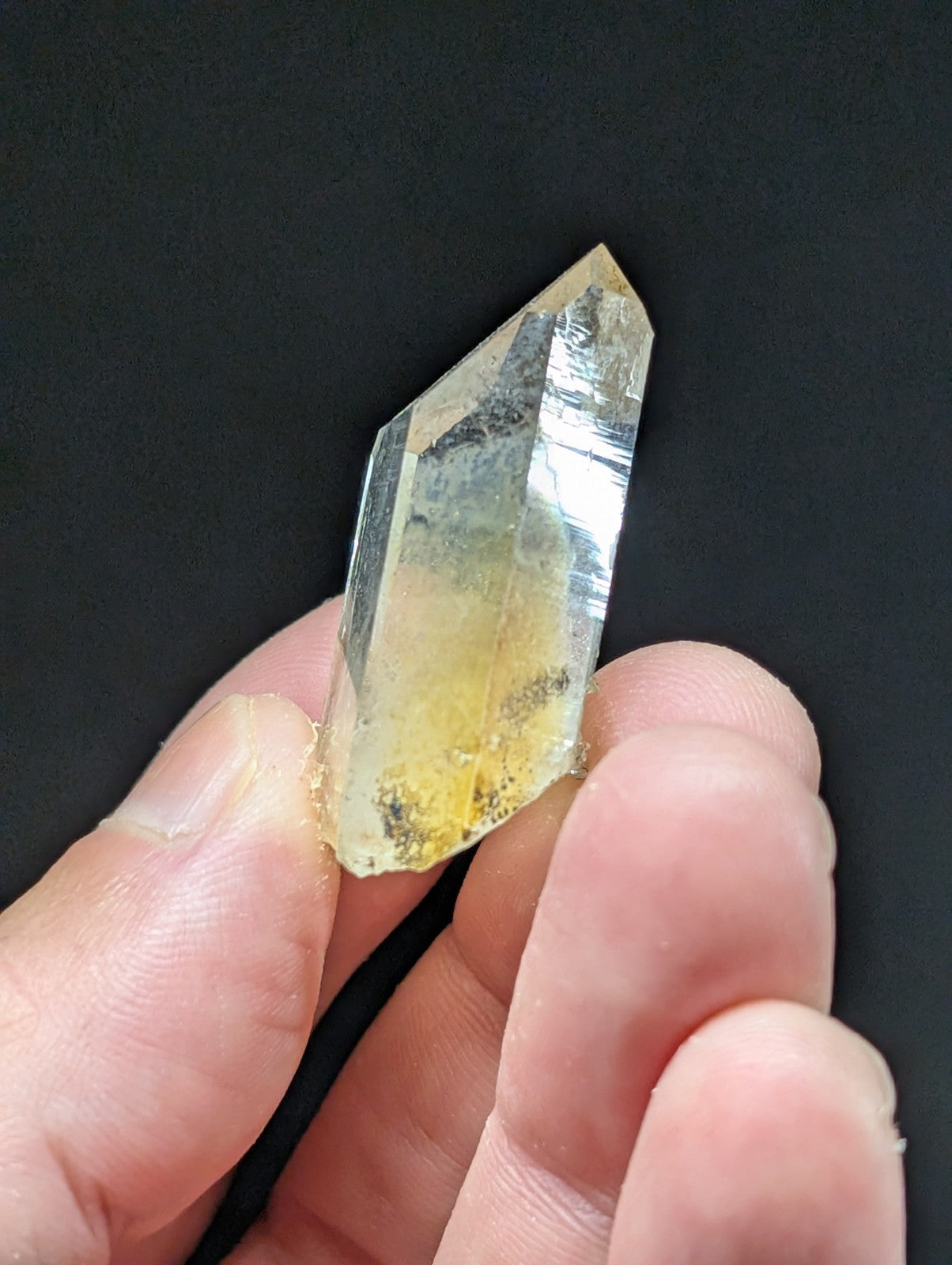A translucent yellowish quartz crystal with a pointed tip and visible internal inclusions, held gently between fingers.