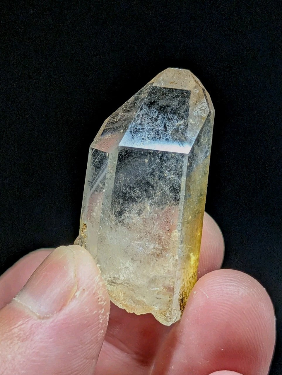 A translucent yellowish quartz crystal with a pointed tip and visible internal inclusions, held gently between fingers.