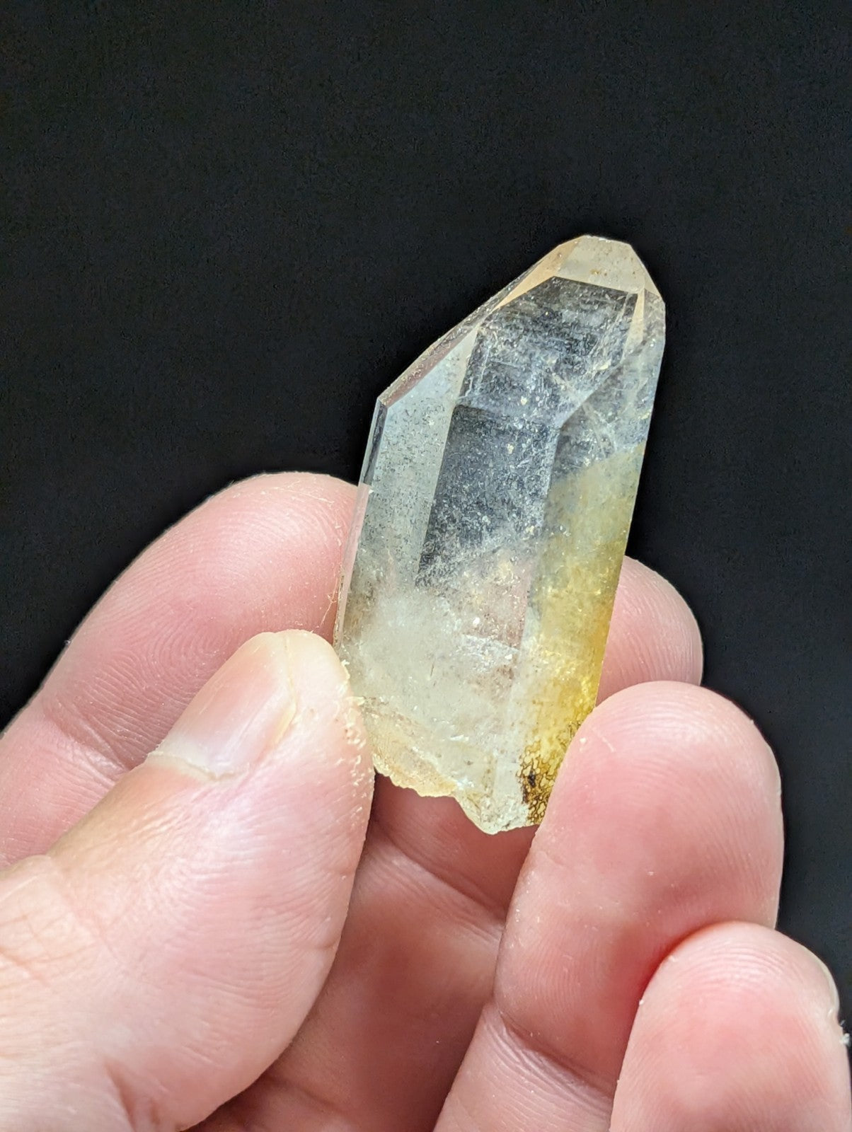 A translucent yellowish quartz crystal with a pointed tip and visible internal inclusions, held gently between fingers.