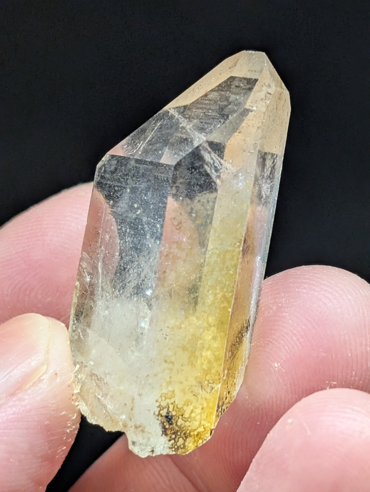 A translucent yellowish quartz crystal with a pointed tip and natural inclusions, held gently between fingers.