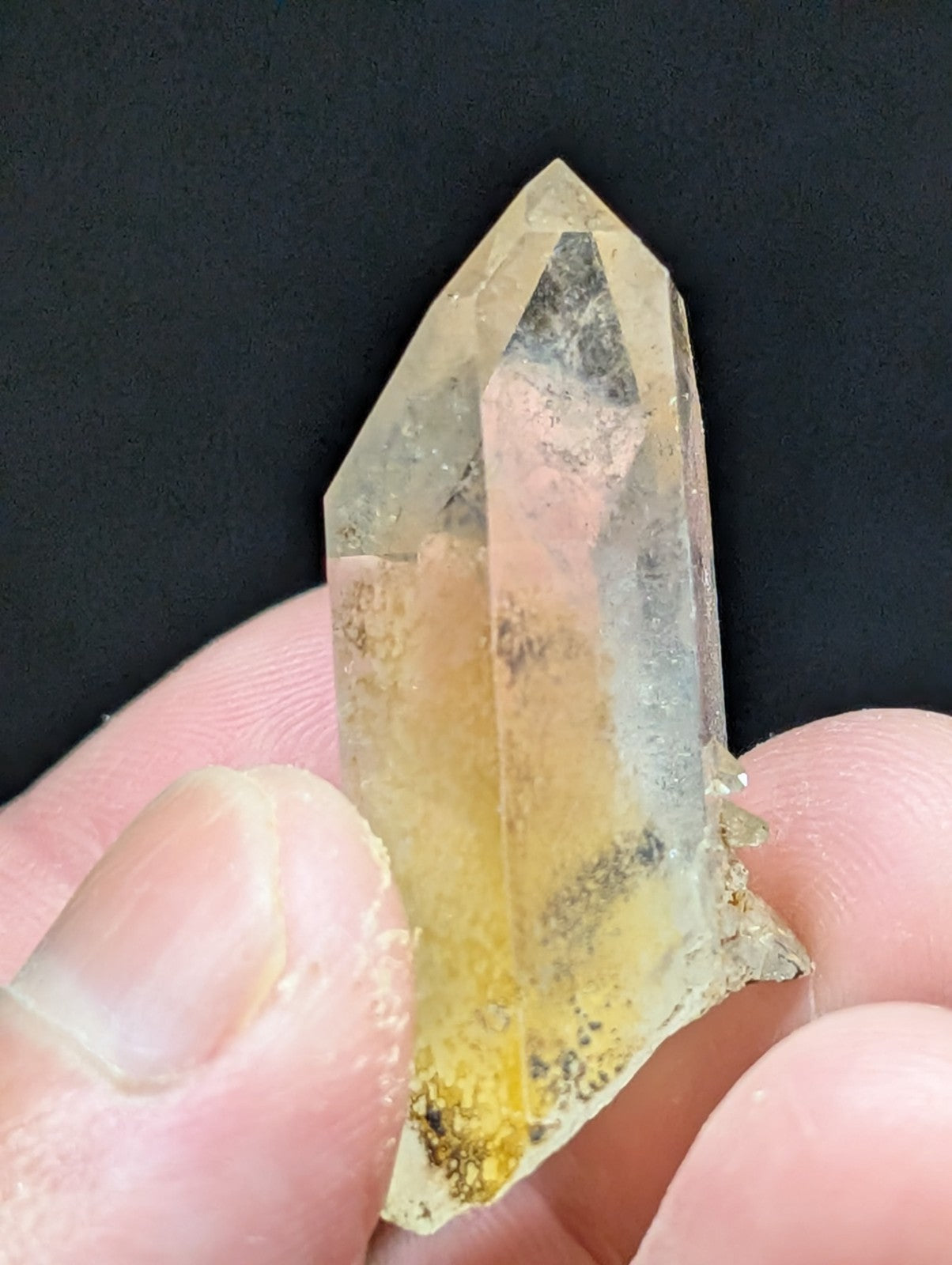 A translucent yellowish quartz crystal with natural inclusions and a pointed, faceted tip.