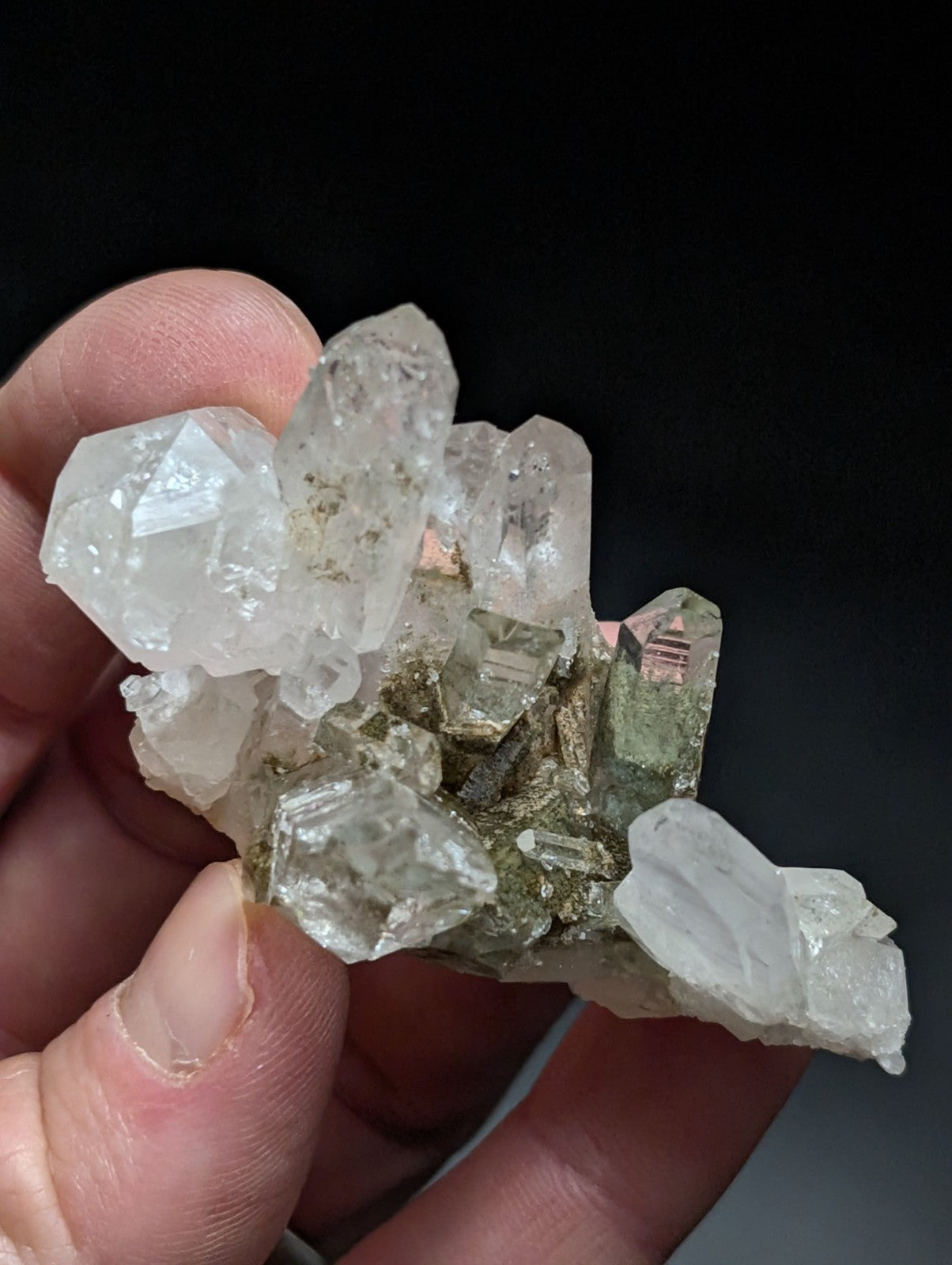 A translucent quartz crystal cluster with a metallic greenish base, held gently in someone’s hand.