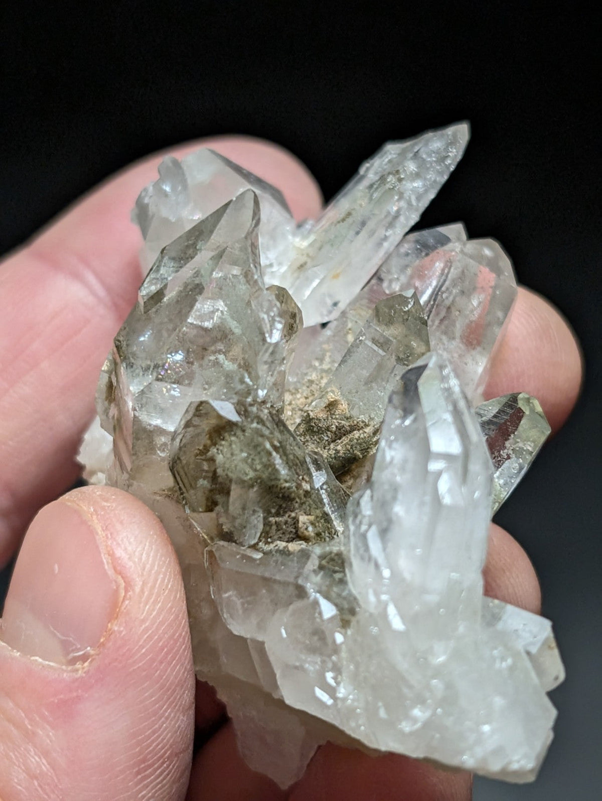 A translucent, clear quartz crystal cluster with sharp, pointed facets and a central patch of greenish mineral residue.