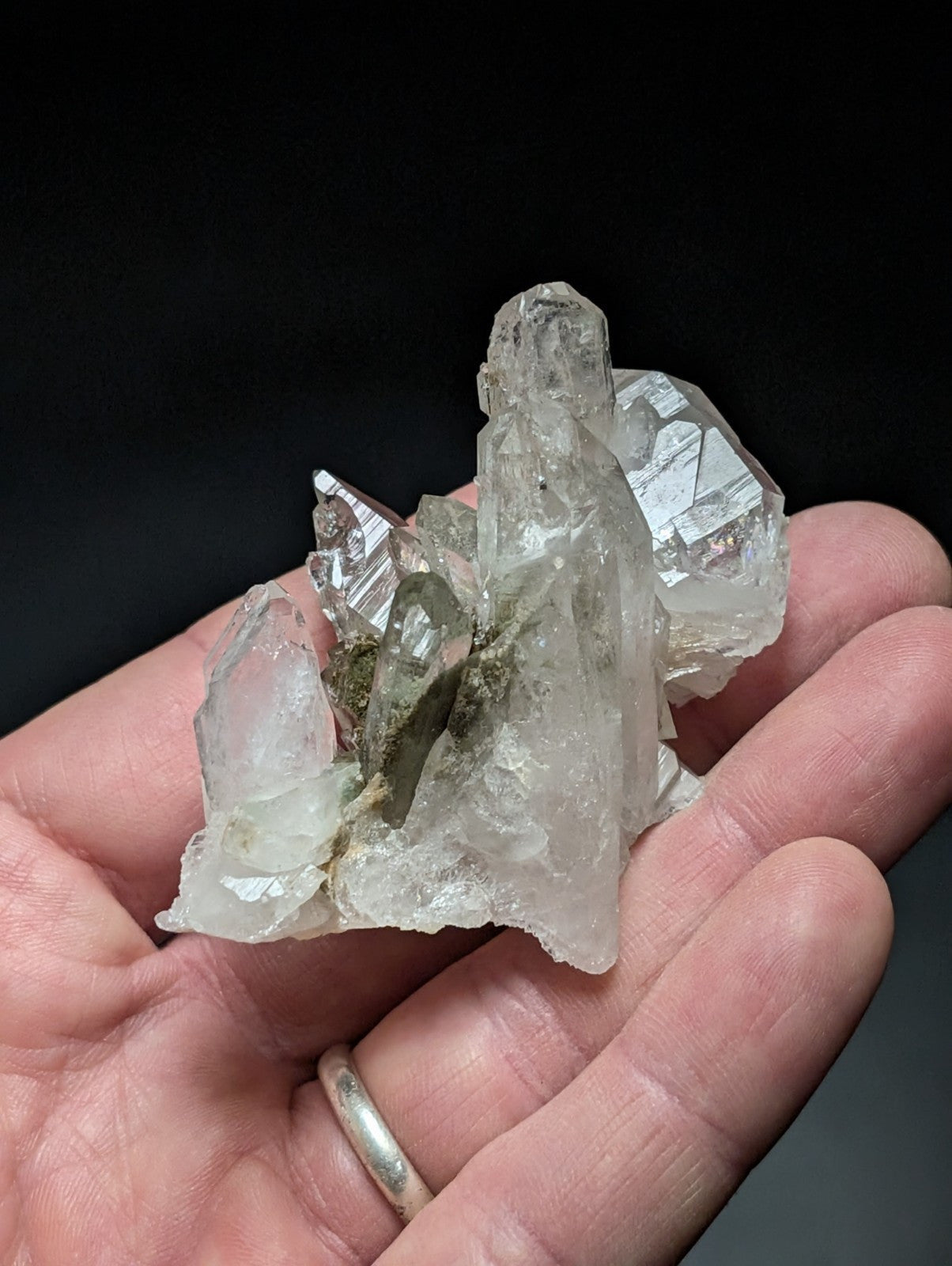A translucent, clear quartz crystal cluster with sharp facets and a few dark green inclusions.