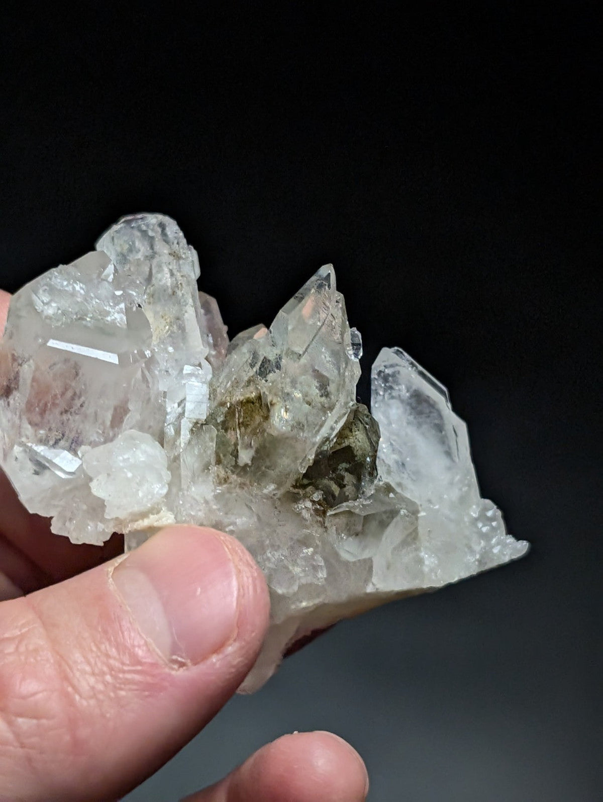 A cluster of clear, translucent quartz crystals with sharp facets and a central greenish mineral inclusion.