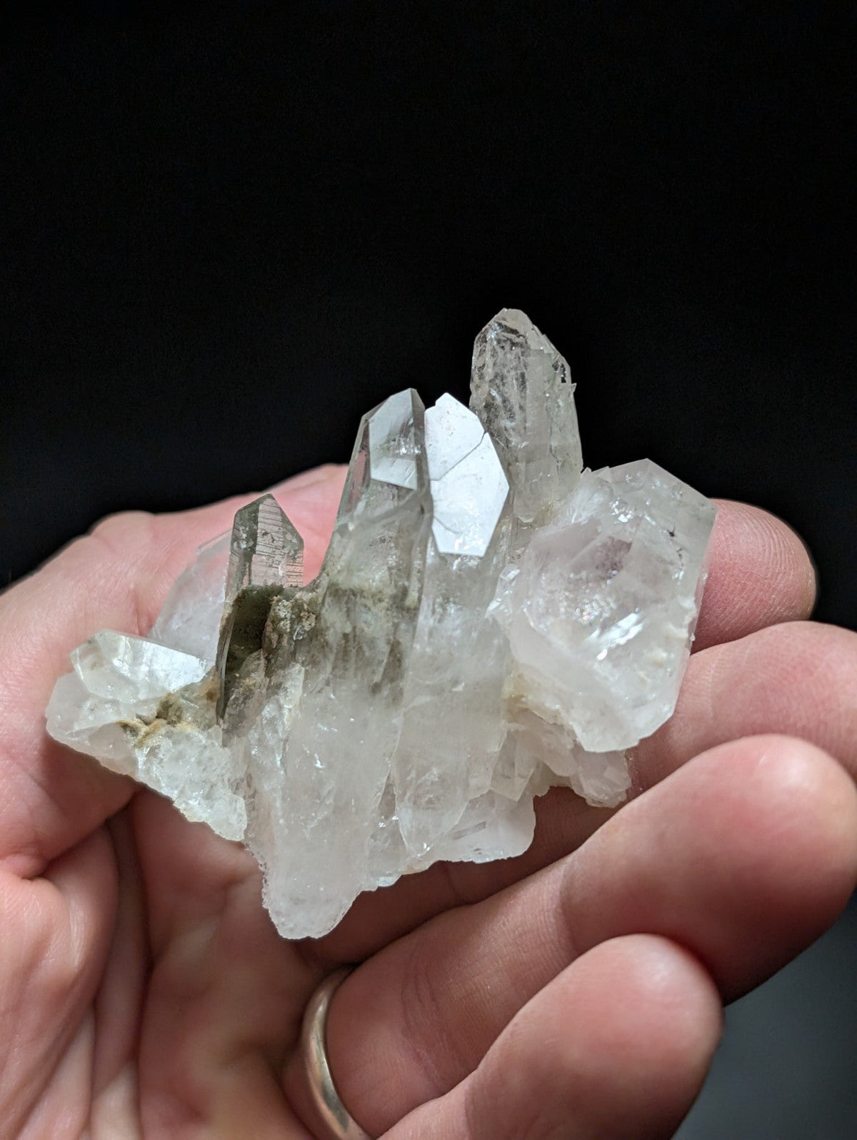 A translucent, clear quartz crystal cluster with sharp facets and a few darker mineral inclusions.