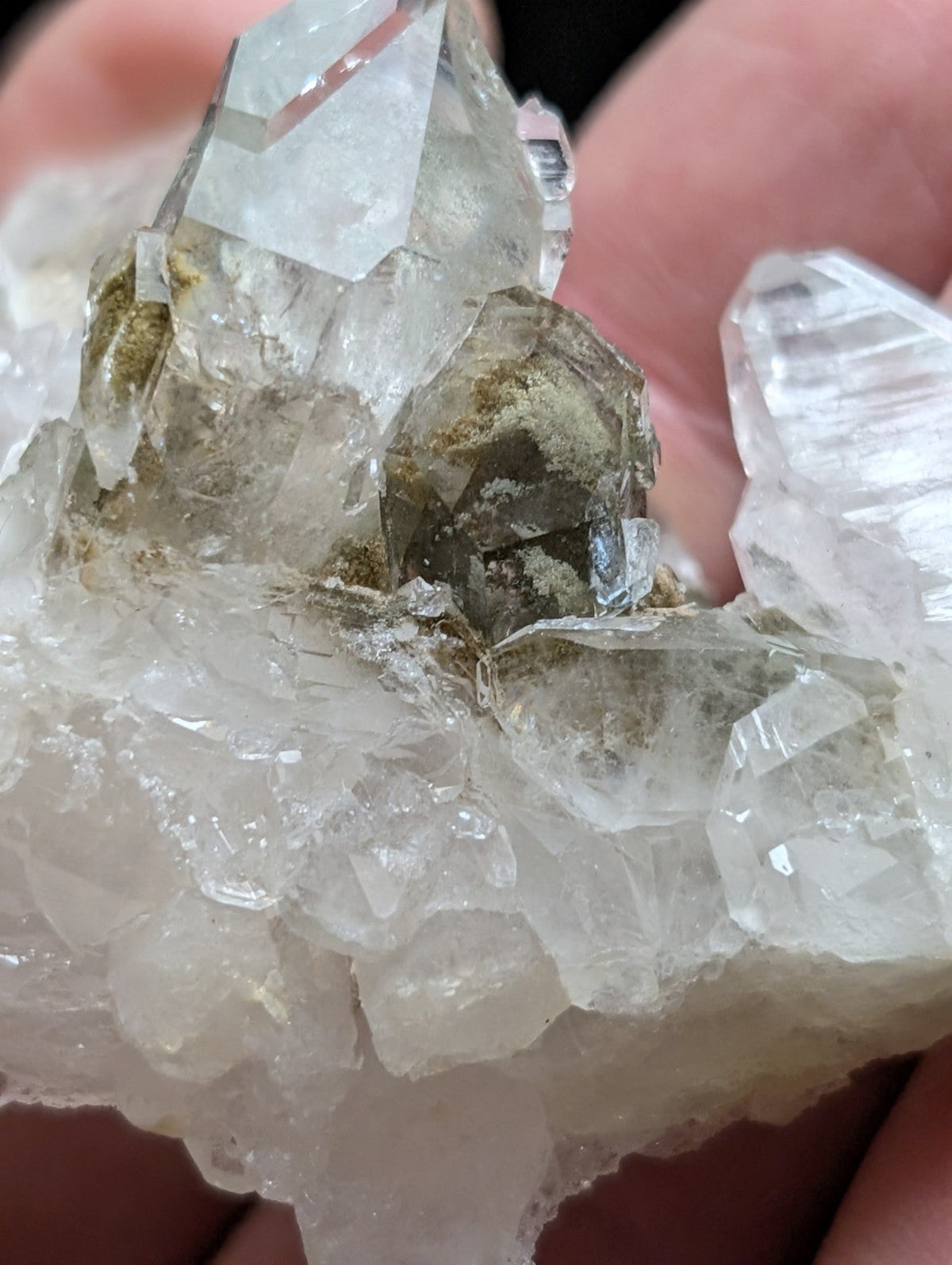 A cluster of clear, faceted quartz crystals with some exhibiting a faint greenish tint and visible mineral inclusions.