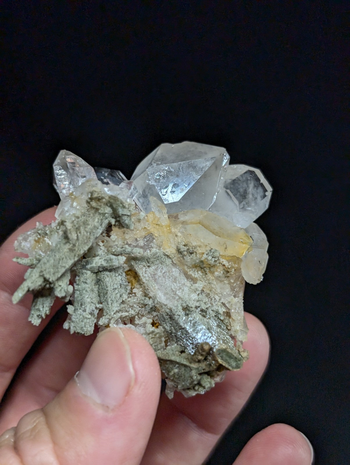 A cluster of clear, faceted quartz crystals growing from a grayish-green mineral matrix.
