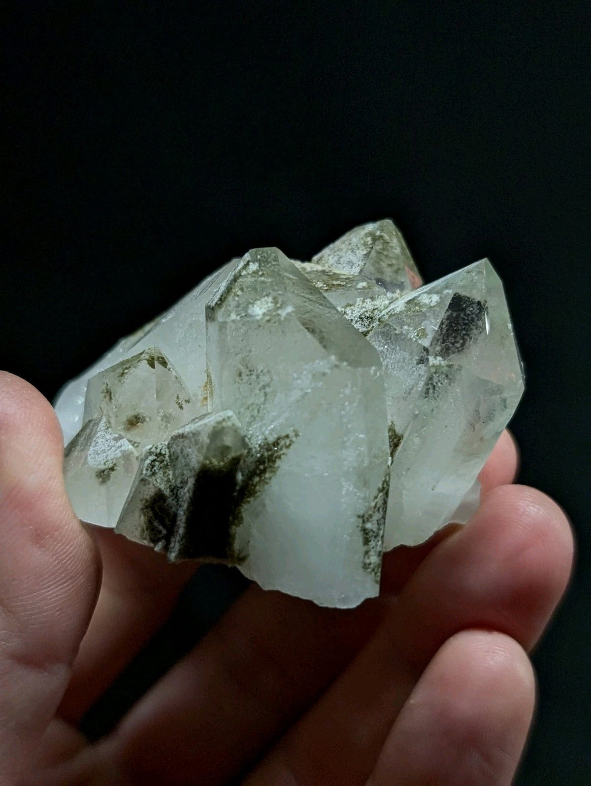 A translucent quartz crystal cluster with clear, faceted points and dark inclusions.