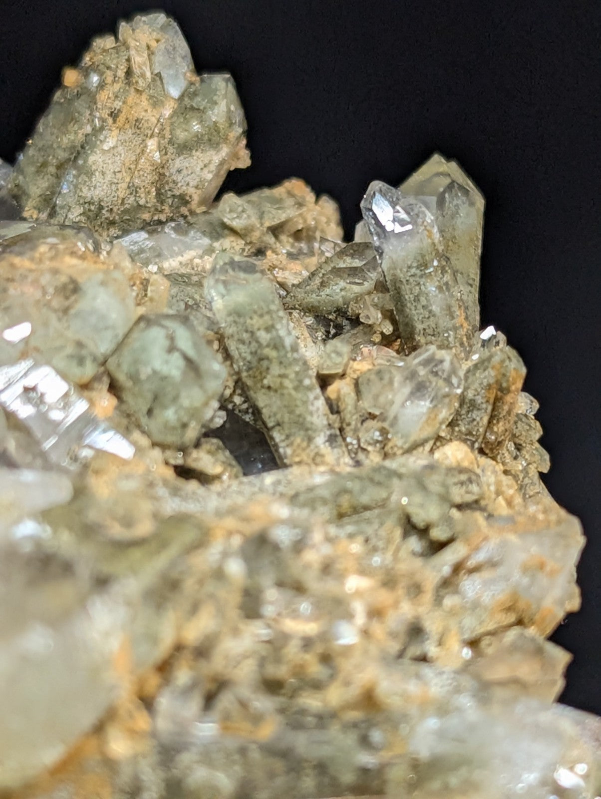 A cluster of translucent greenish quartz crystals growing from a rough, earthy matrix.