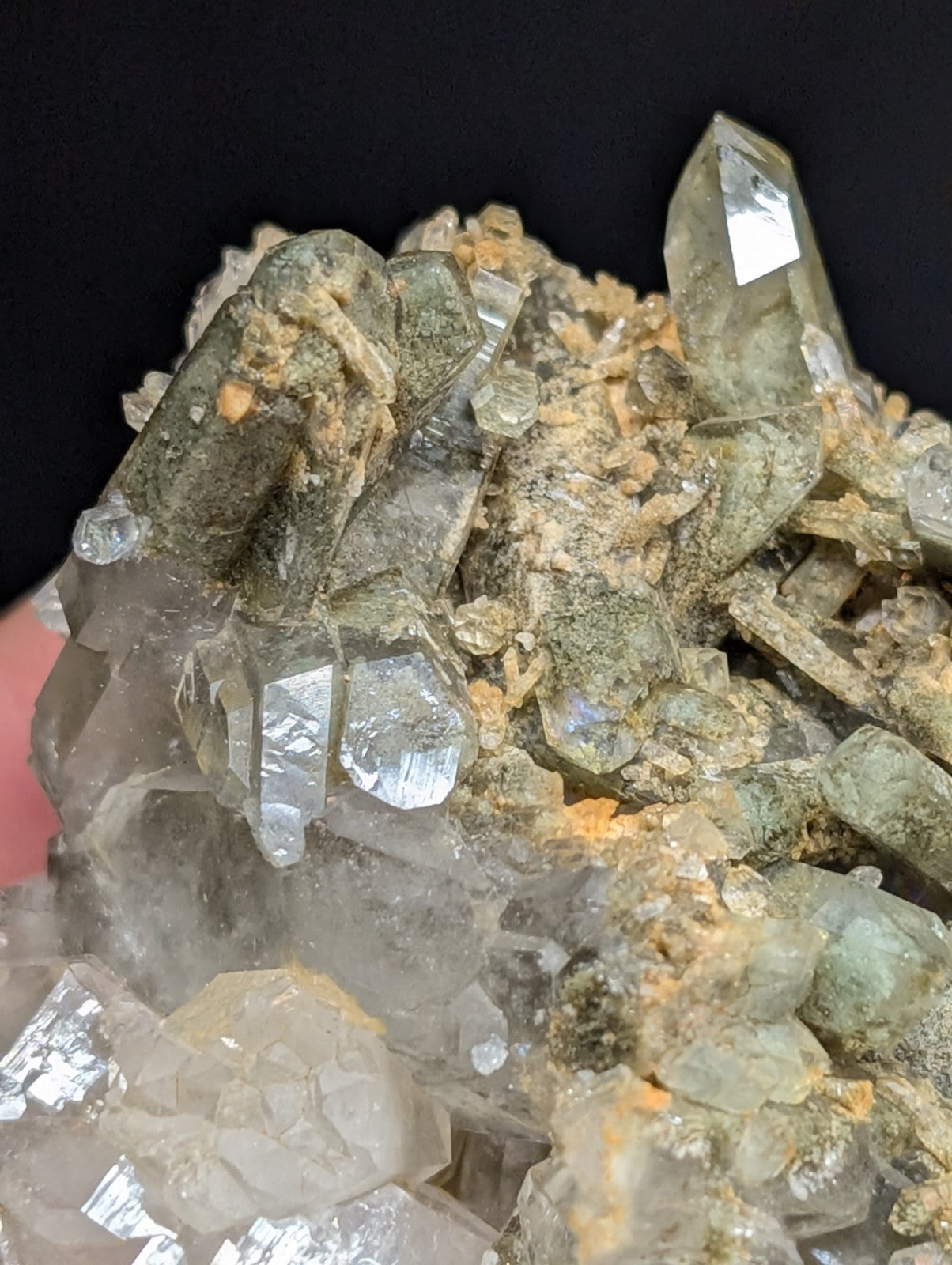 A cluster of translucent green and clear quartz crystals with sharp, faceted points emerging from a rough, earthy matrix.