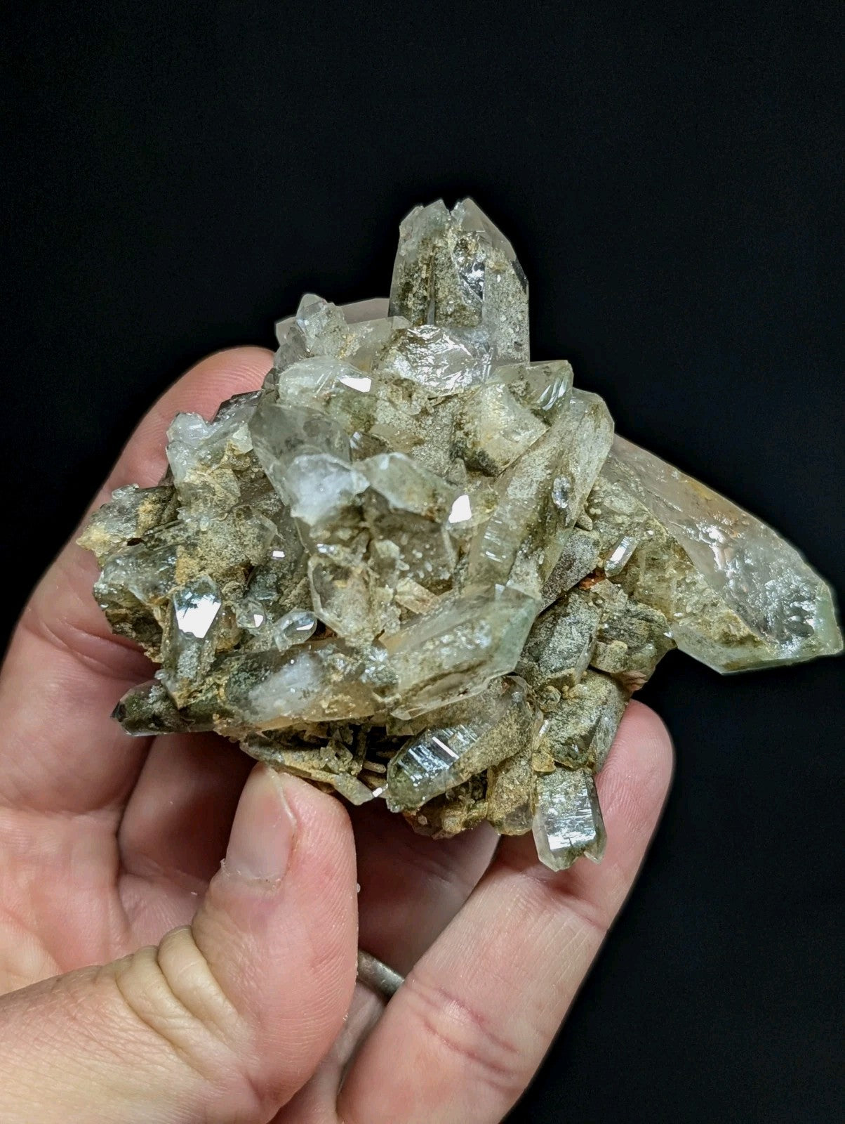 A cluster of translucent quartz crystals with a mix of clear and pale green hues, embedded in a rough, earthy matrix.