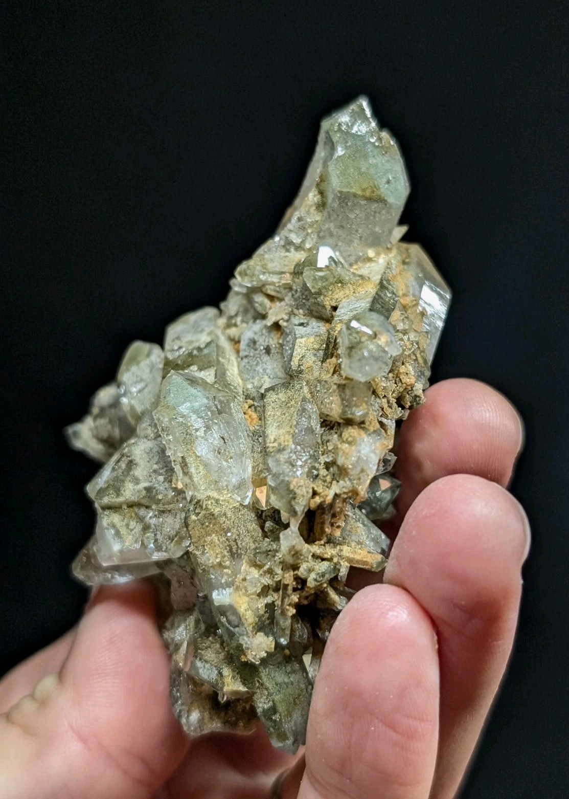 A translucent greenish quartz crystal cluster with sharp, faceted points and a rough, earthy matrix.
