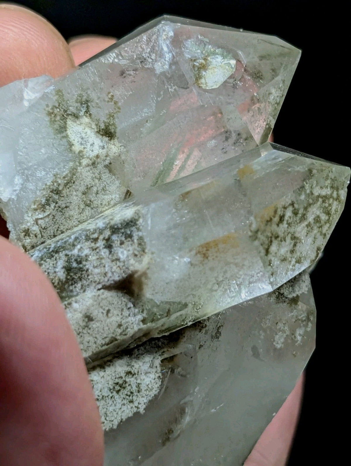 A translucent, clear quartz crystal cluster with greenish mineral inclusions and a faceted, geometric structure.
