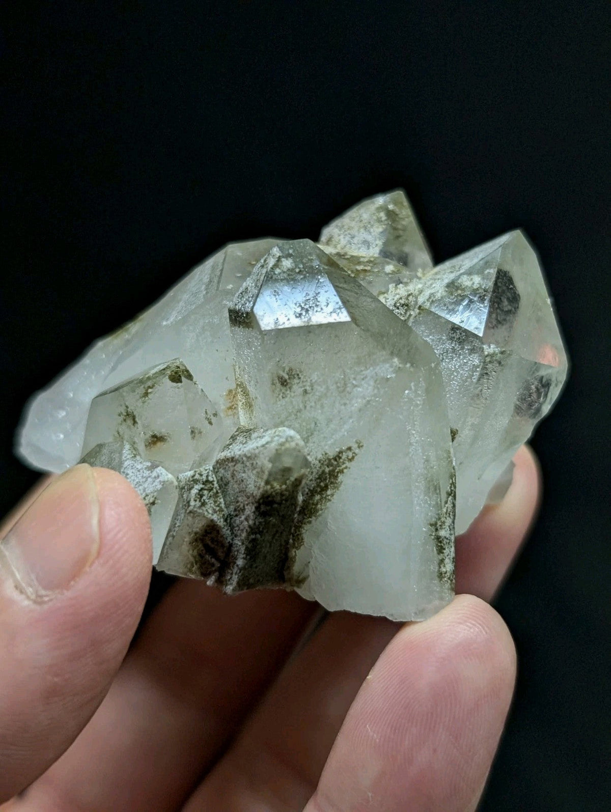 A translucent, clear quartz crystal cluster with natural greenish-brown inclusions and sharp geometric facets.