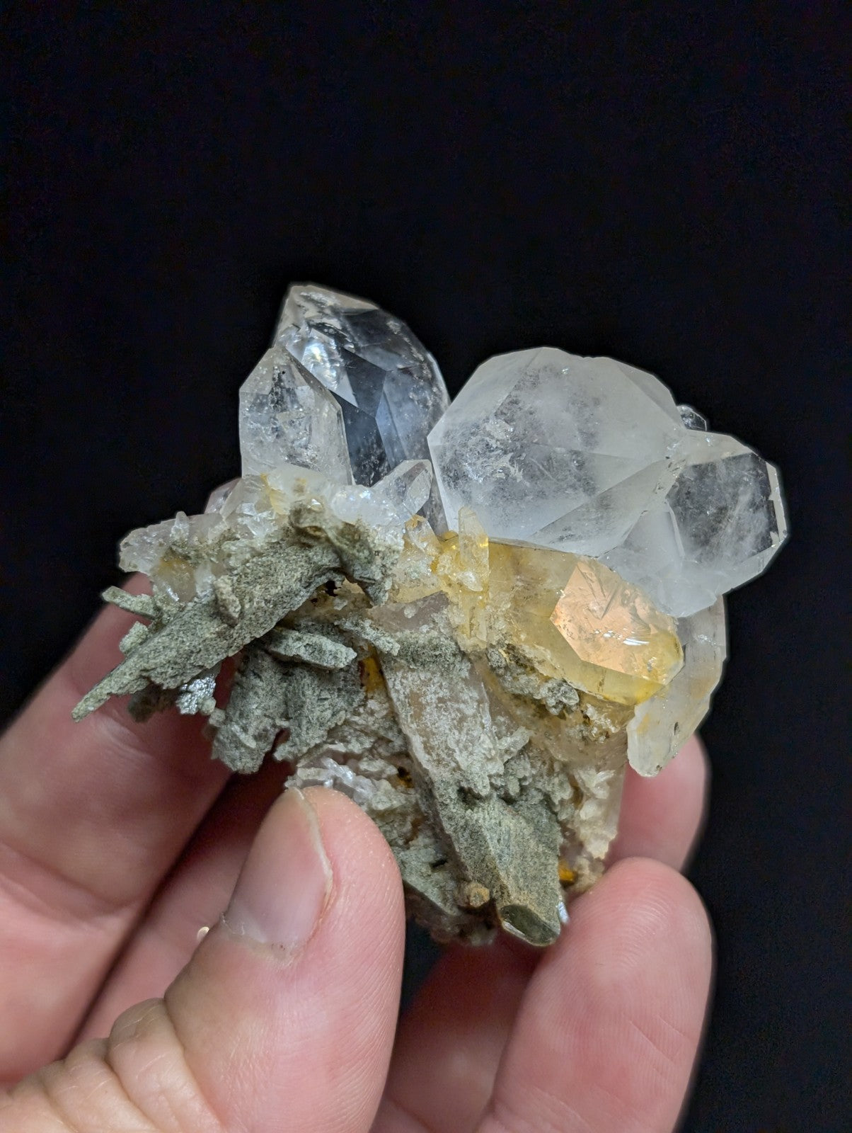 A translucent quartz crystal cluster with clear, faceted points and a yellowish-orange inclusion nestled atop a gray mineral matrix.