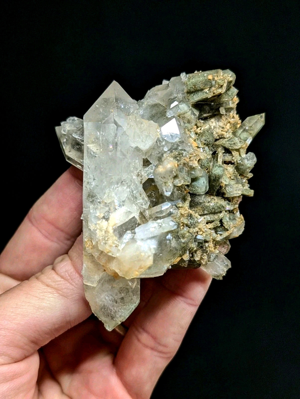 A translucent quartz crystal cluster with clear, faceted points and earthy greenish-brown matrix.