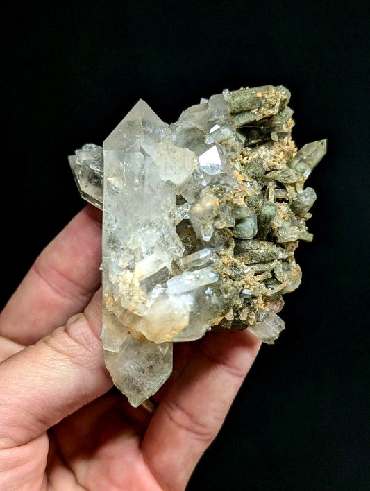 A translucent quartz crystal cluster with clear, faceted points and earthy greenish-brown matrix.