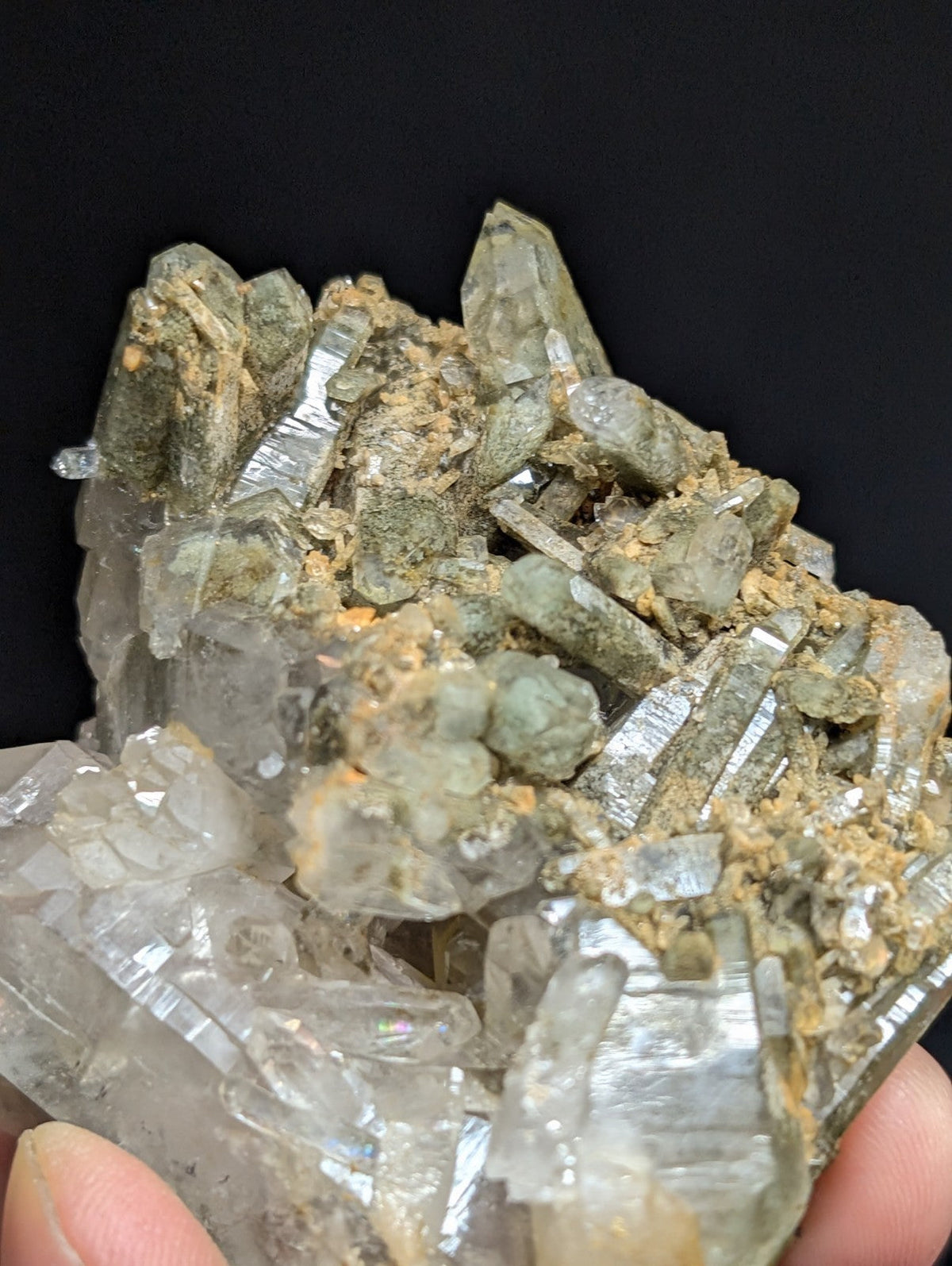 A cluster of translucent greenish quartz crystals with metallic sheen, embedded in a matrix of earthy brown and gray mineral debris.