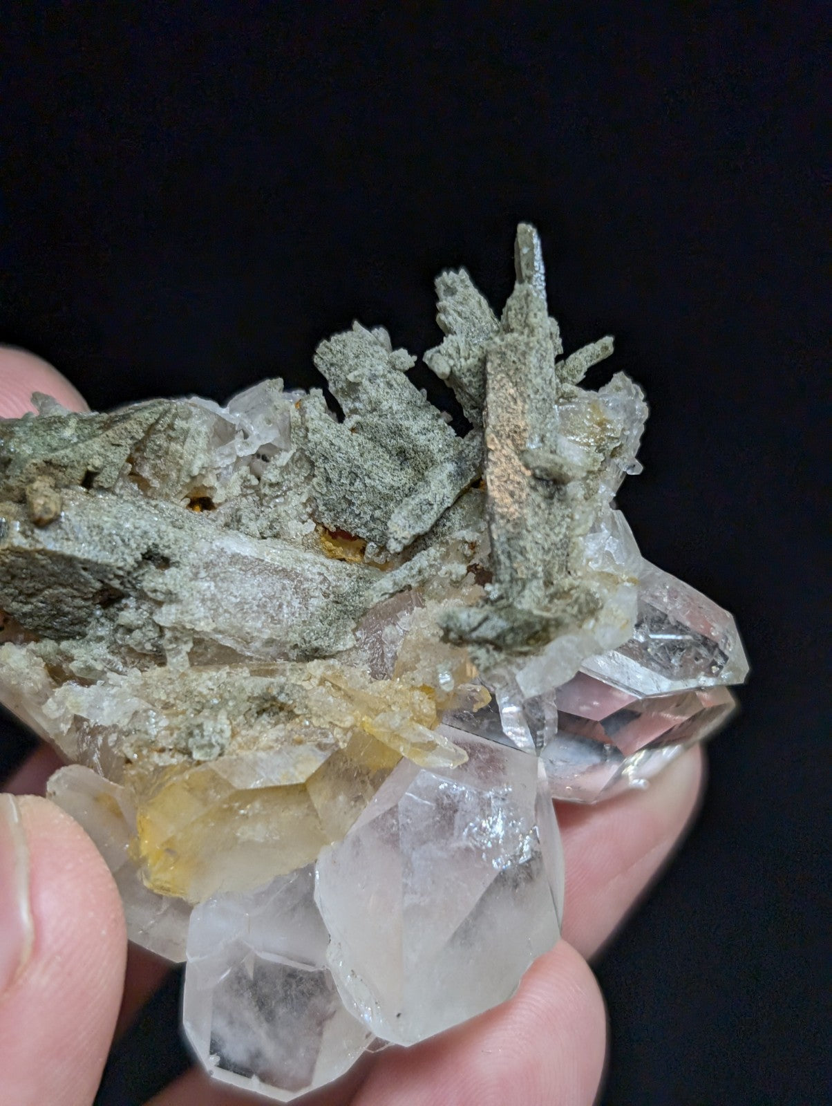 A cluster of translucent quartz crystals with a grayish, mossy matrix and hints of yellow inclusions.