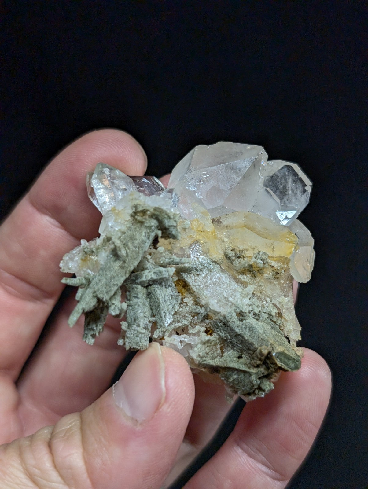 A translucent quartz crystal cluster with greenish-gray matrix and yellowish inclusions, held gently in a hand.